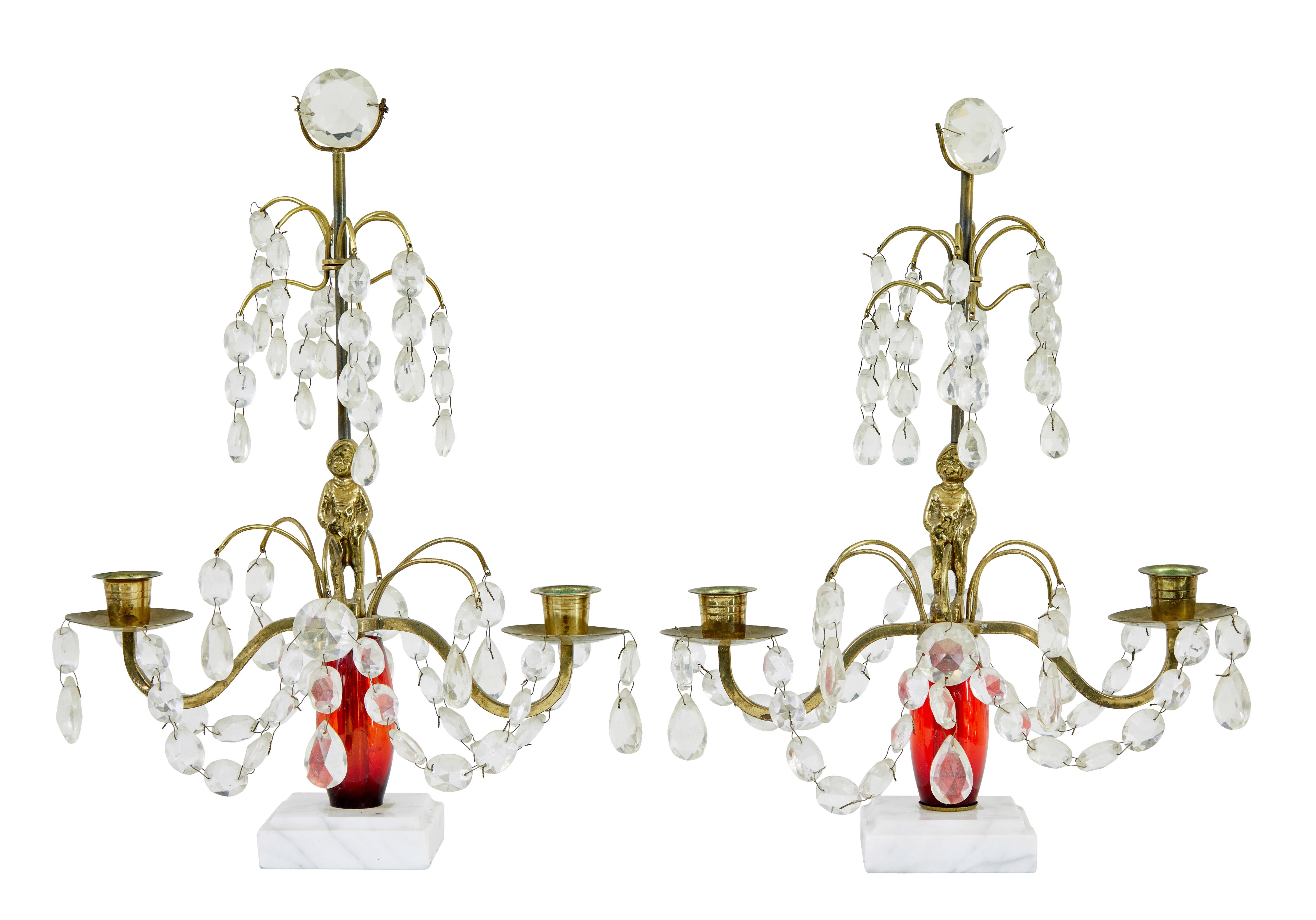 Paar Kandelaber aus geschliffenem Glas und Marmor aus der Mitte des 20. Jahrhunderts, um 1960.

Roter Hauptstiel aus Kunststoff mit einer Messingfigur eines Jungen in der Mitte.  2 Messingarme mit 2 Kerzenhalterungen. Geschliffene Glastropfen, auf