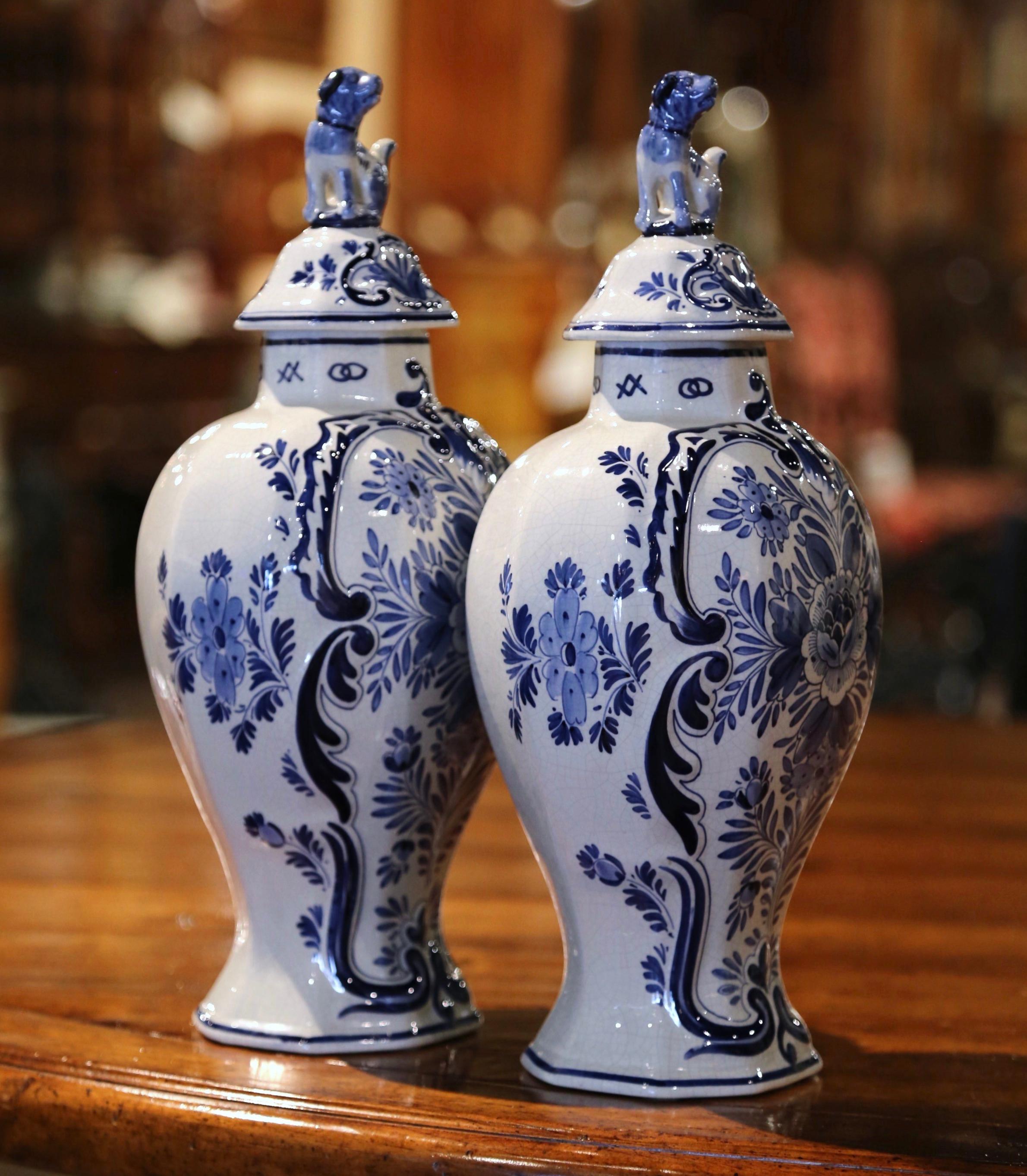 These porcelain ginger jars with lid were created in Holland, circa 1950. Both vases feature a hand painted center medallion decorated with floral and foliage motifs in the traditional blue and white Delft palette. The traditional jars are further