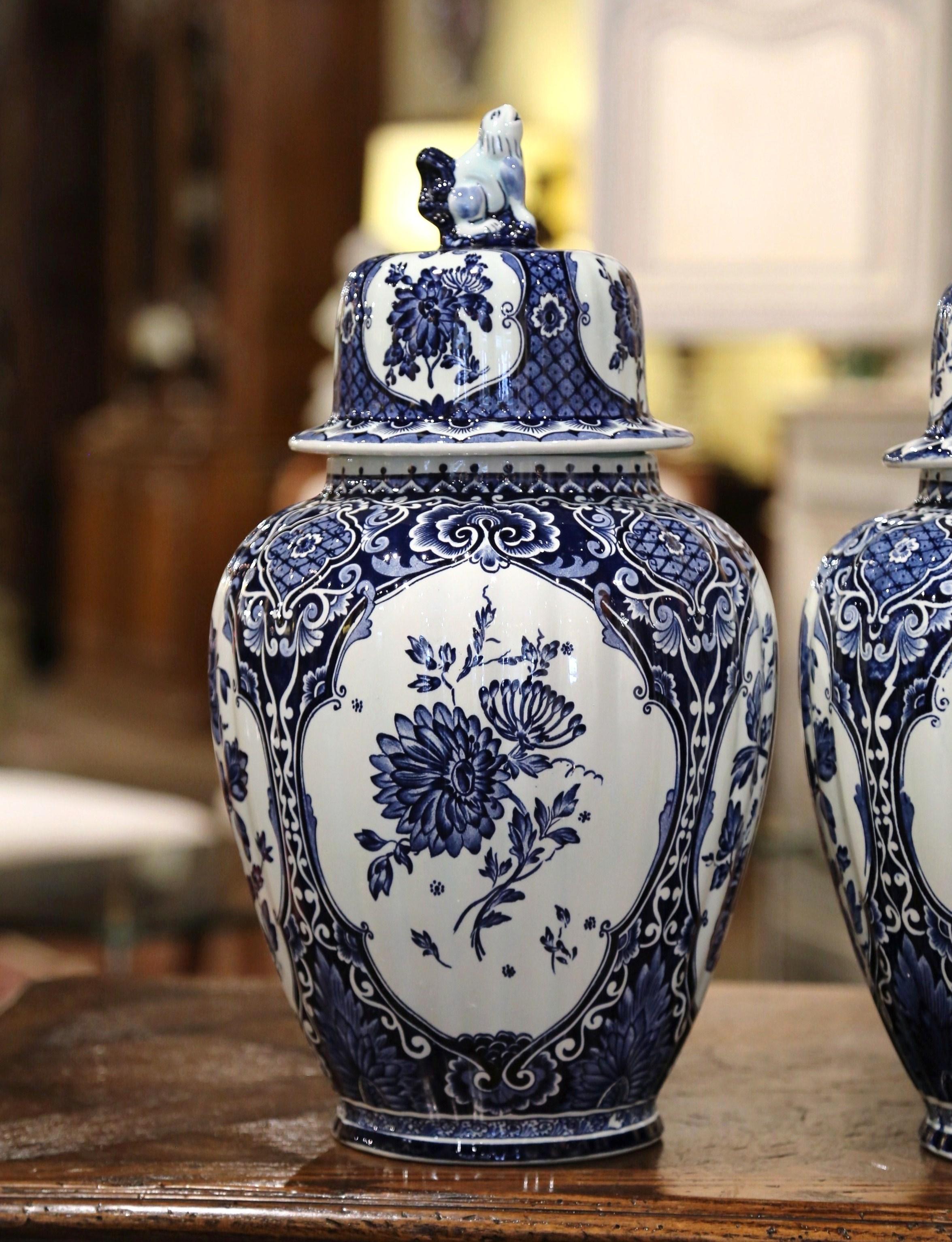 Place this elegant pair of antique ceramic ginger jars on a mantel, crafted in Holland, circa 1940, the large faience potiches feature hand painted medallions with Classic Dutch flower and foliage decor. The traditional blue and white jars are round