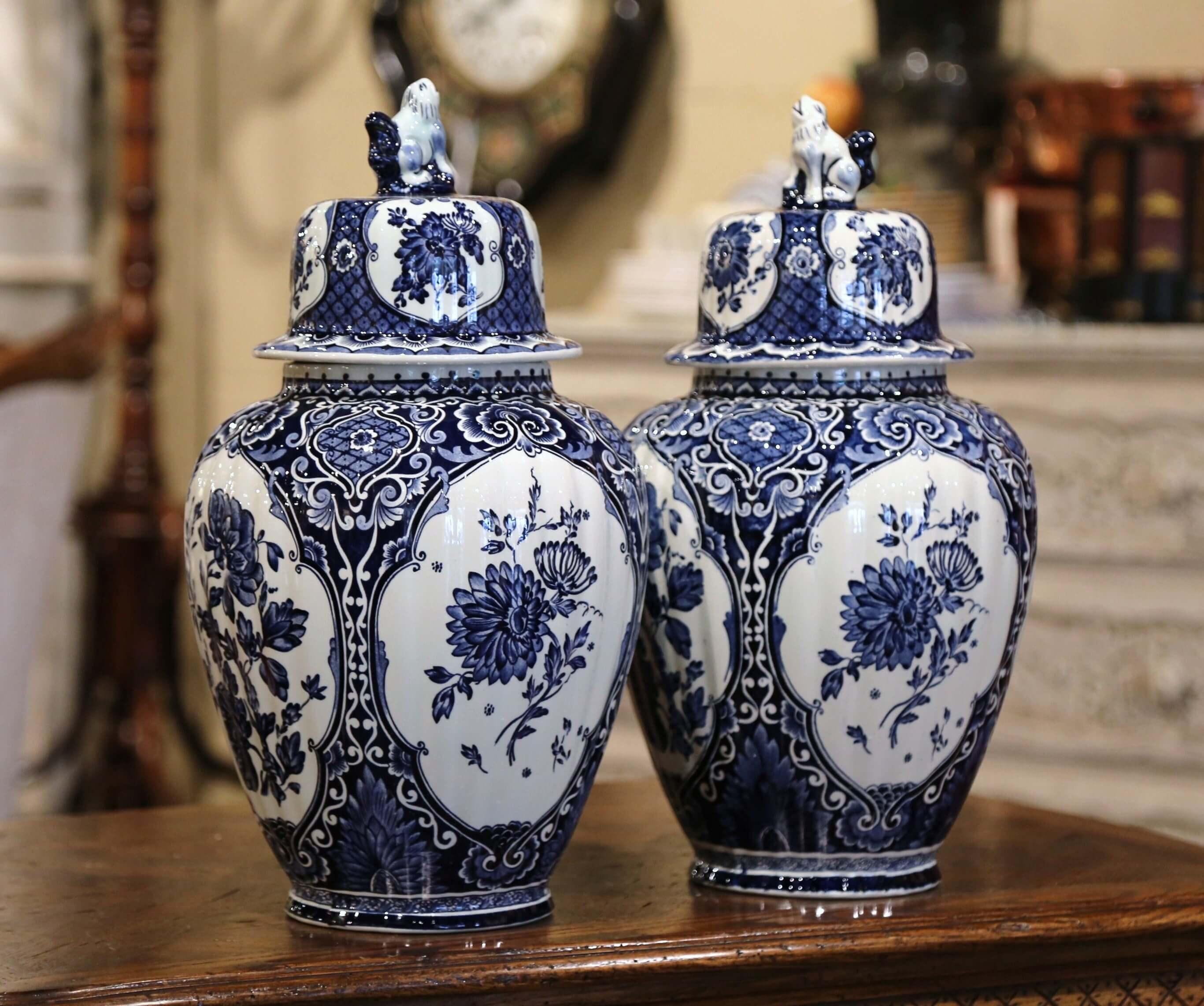 Place this elegant pair of antique ceramic ginger jars on a mantel or a console in entryway. Crafted in Holland, circa 1960, the traditional blue and white jars are round in shape and have a cone lid embellished with dog figure at the top; each