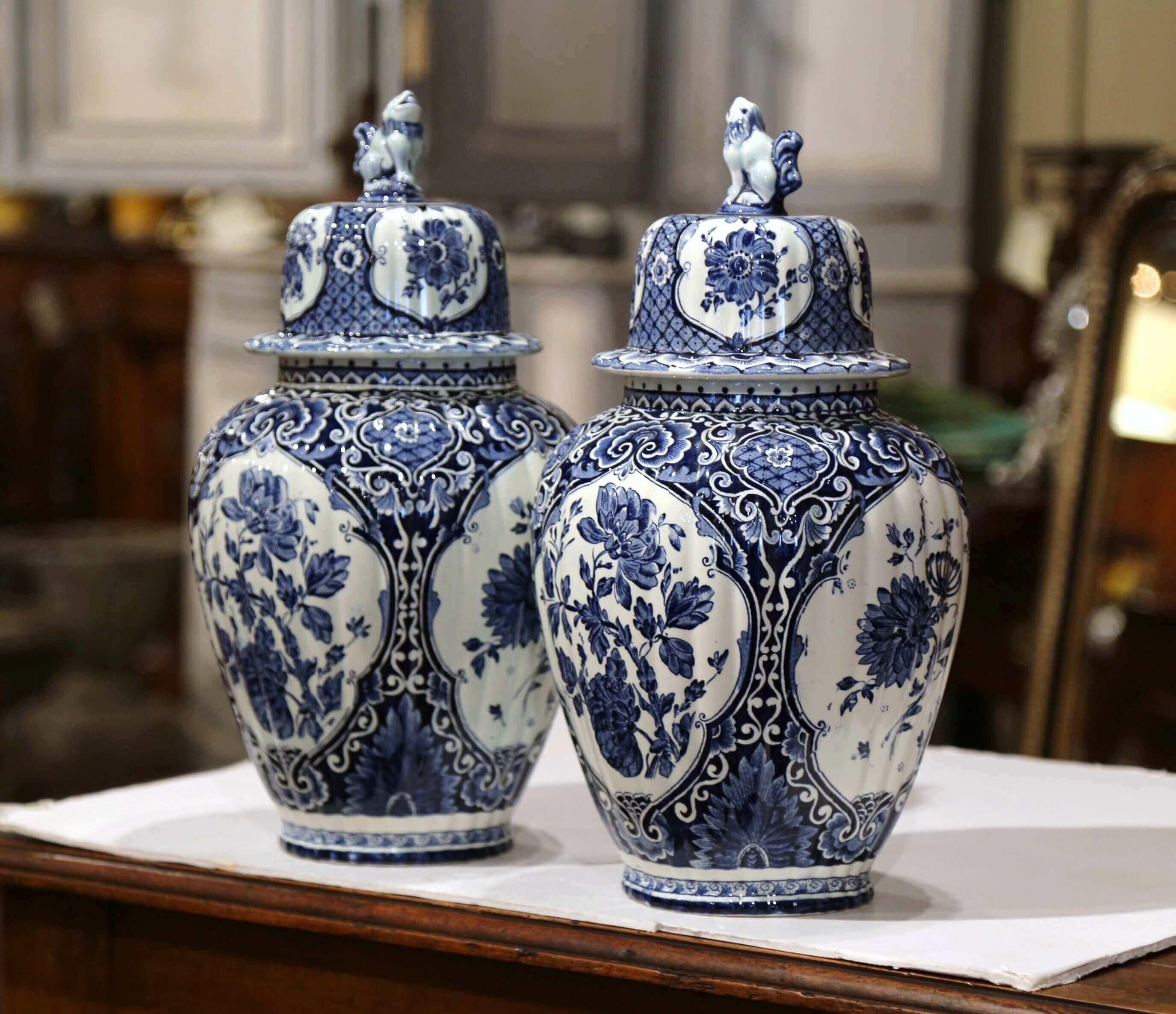 Place this elegant pair of antique ceramic ginger jars on a mantel or a console in entryway. Crafted in Holland, circa 1960, the traditional blue and white jars are round in shape and have a cone lid embellished with dog figure at the top; each