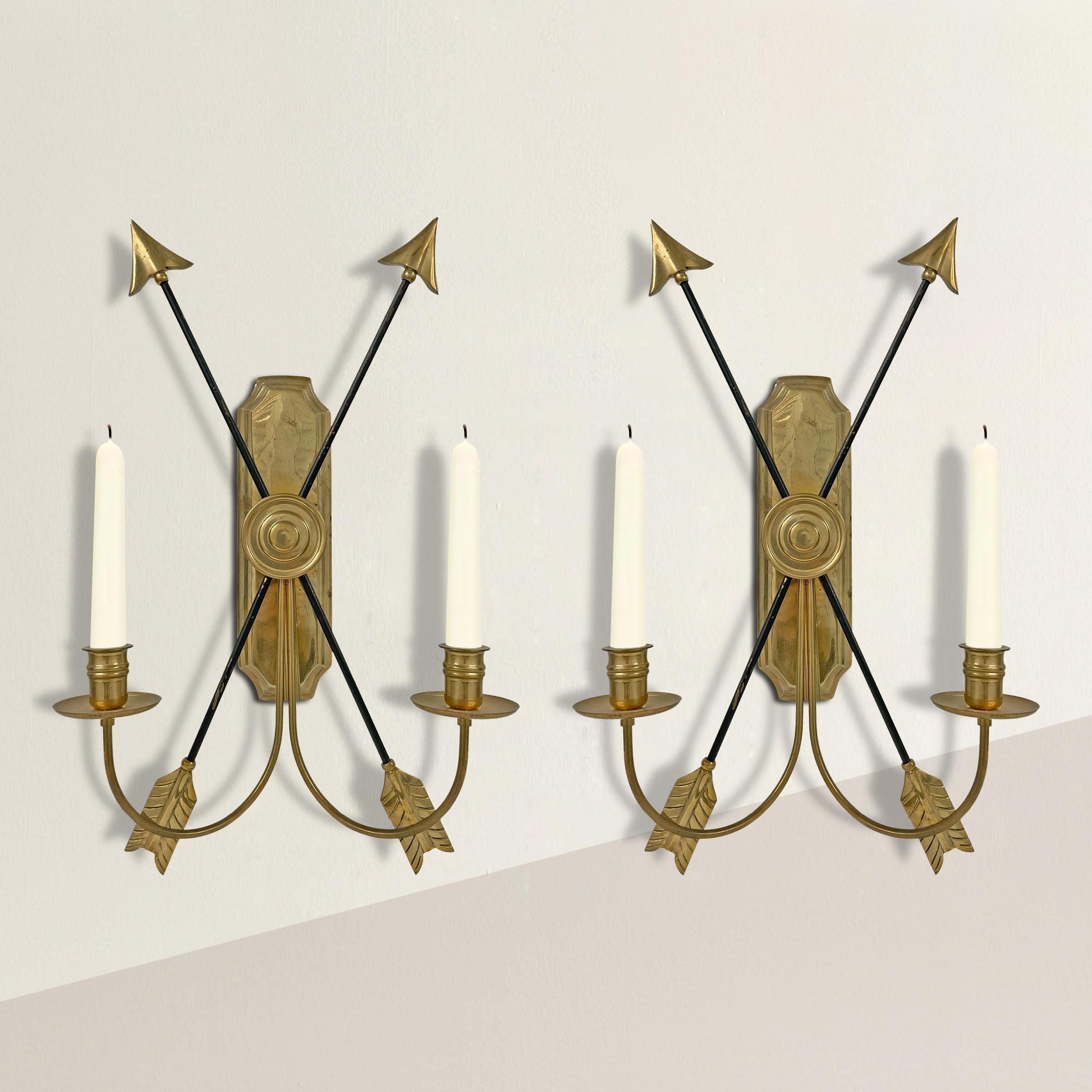 A chic pair of mid-20th century Empire-style brass candle sconces, each with two arms and two crossed arrows. Perfect in your entry flanking a mirror, or down the hallway in your home.