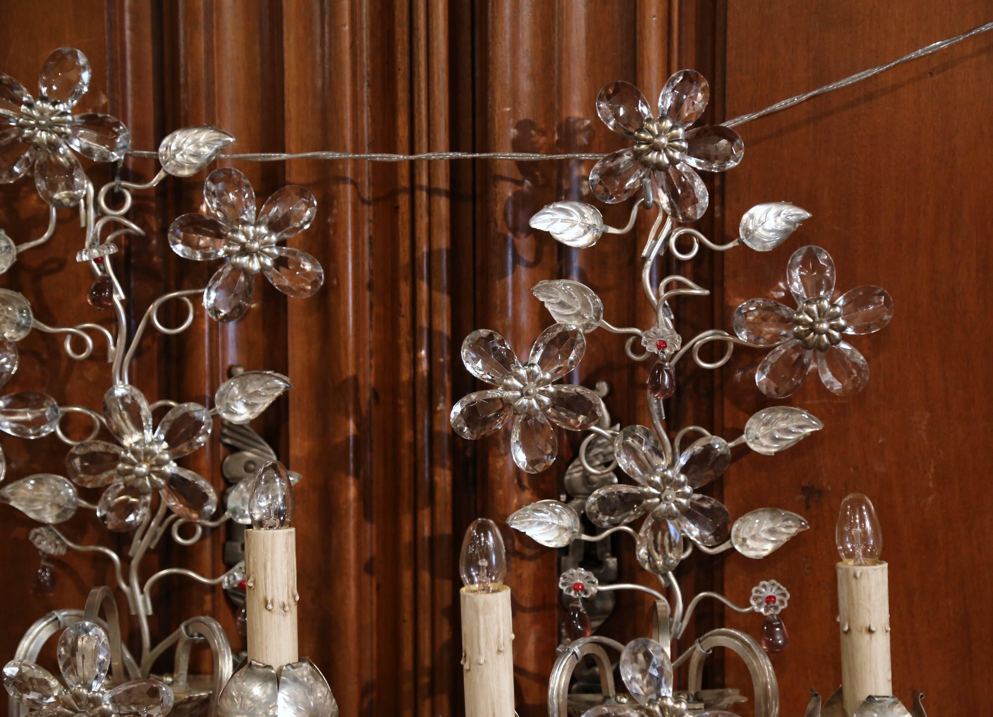 This pair of elegant, vintage Bagues wall lights were created in Paris, France, circa 1950. Each of the elaborate sconces has two lights and features shaped crystal flowers and leaves with silver leaf detail. Both fixtures are in excellent condition