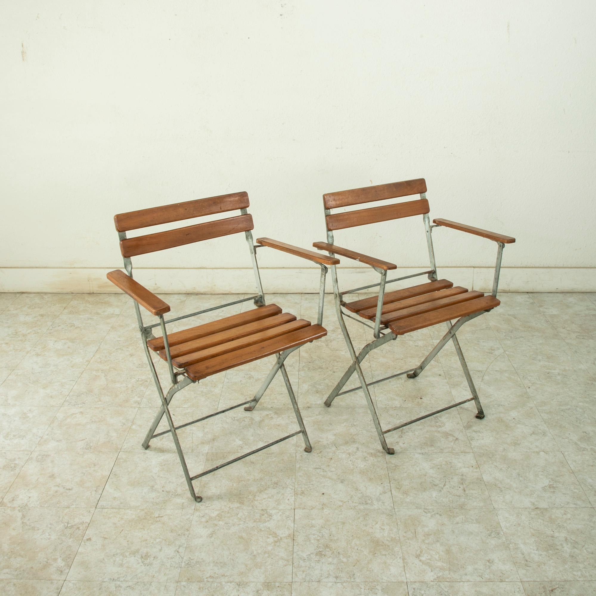 Found in the spa town of Bagnoles de l'Orne in the region of Normandy, France, this pair of mid-century metal bistro armchairs features wooden slats on the seat, seatback, and arms. These chairs fold flat for easier storing. An ideal pair for a