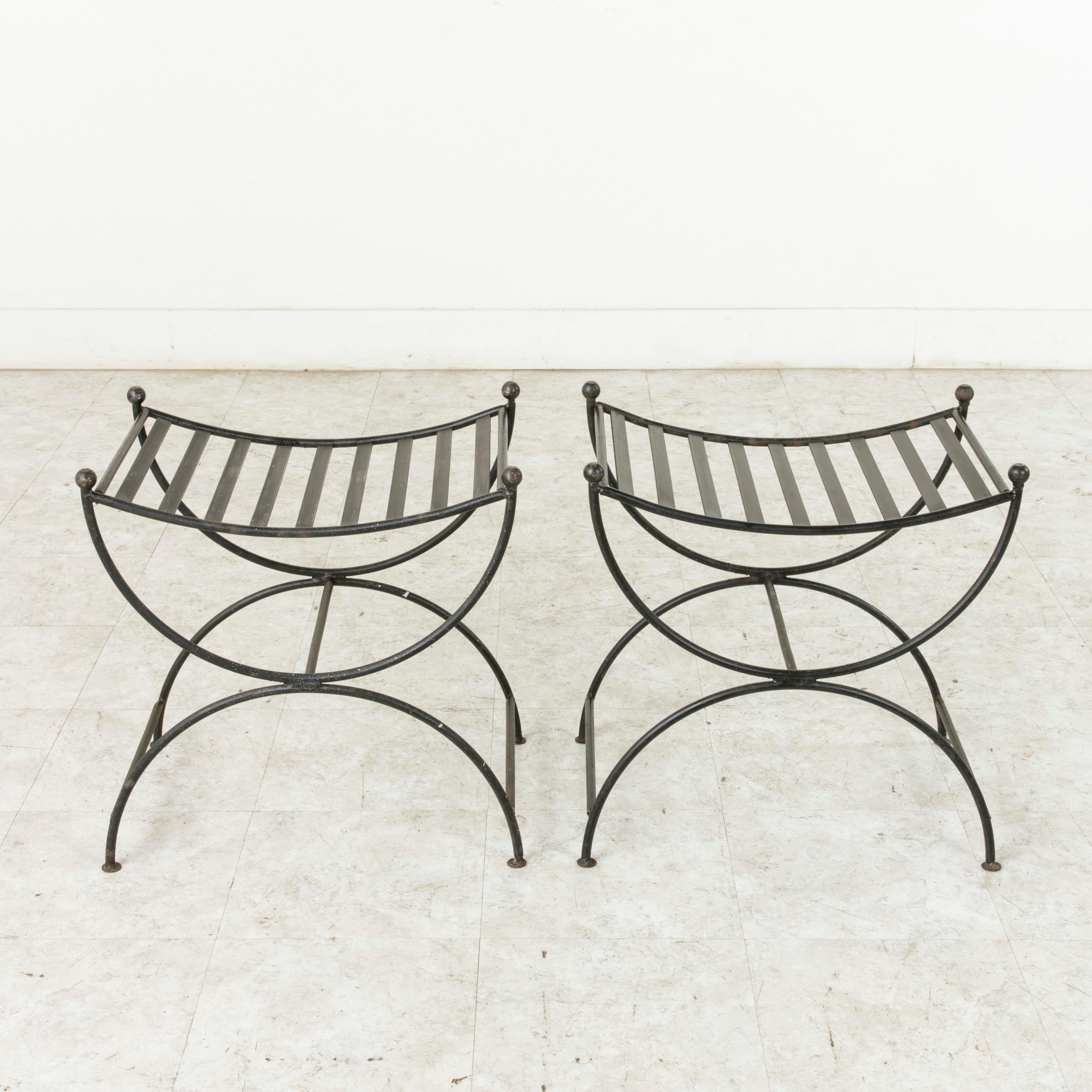 This pair of mid-20th century French iron banquettes, benches, or stools, features a slatted seat supported by opposing half circles that form the legs. Iron bars extend between the legs to provide additional stability. Finished with round iron