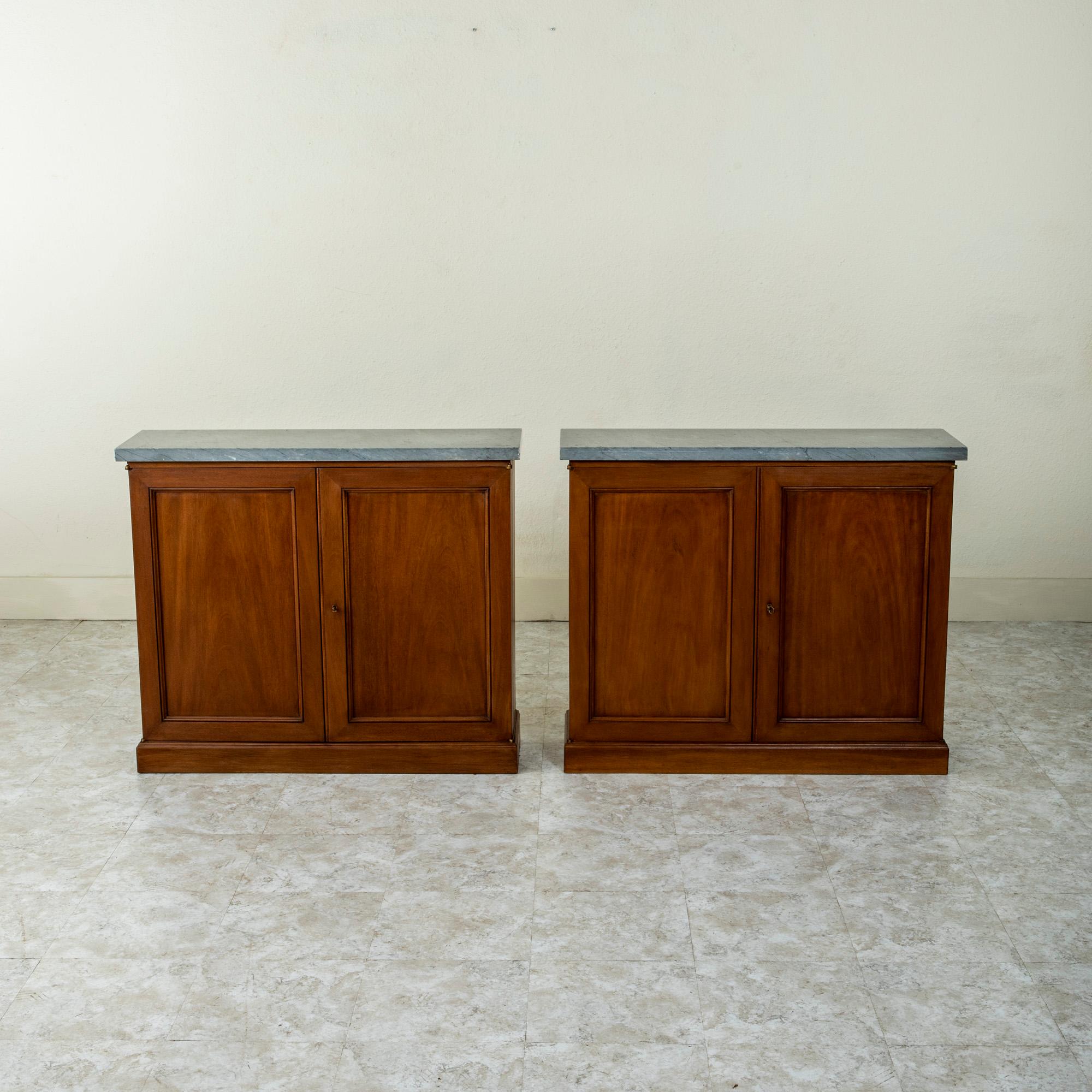 A handsome pair from the Mid-20th Century, these console cabinets are constructed of solid mahogany and feature grey marble tops with black veining. The cabinet doors open to reveal two interior adjustable shelves. Each cabinet has its own key with