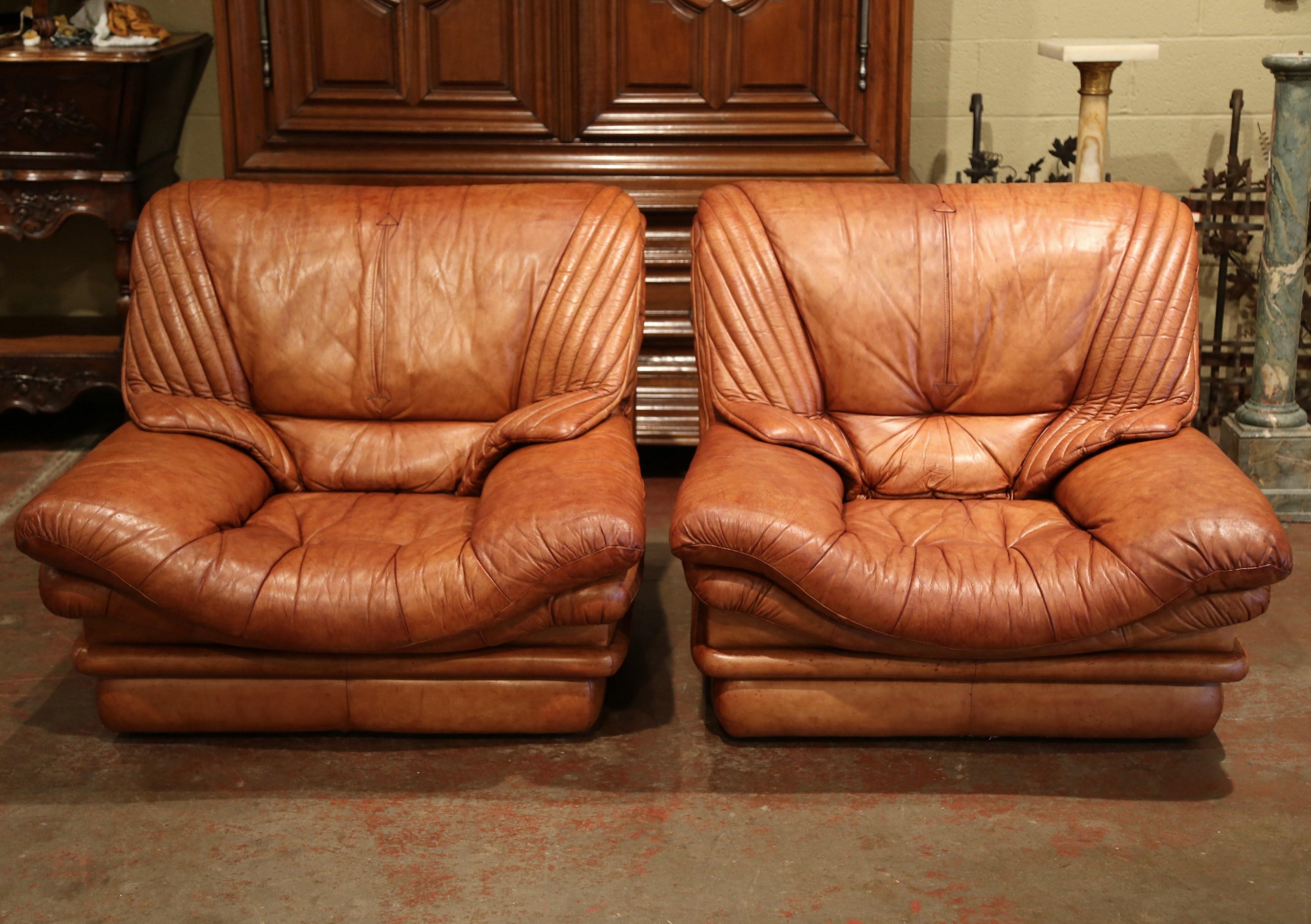 Watch your favorite show or football game in these cozy, vintage Art Deco club armchairs. Crafted in France, circa 1960, the stately, masculine chairs sit on a square plinth base, and feature deep seat, rounded armrests, and wide pitched back. The