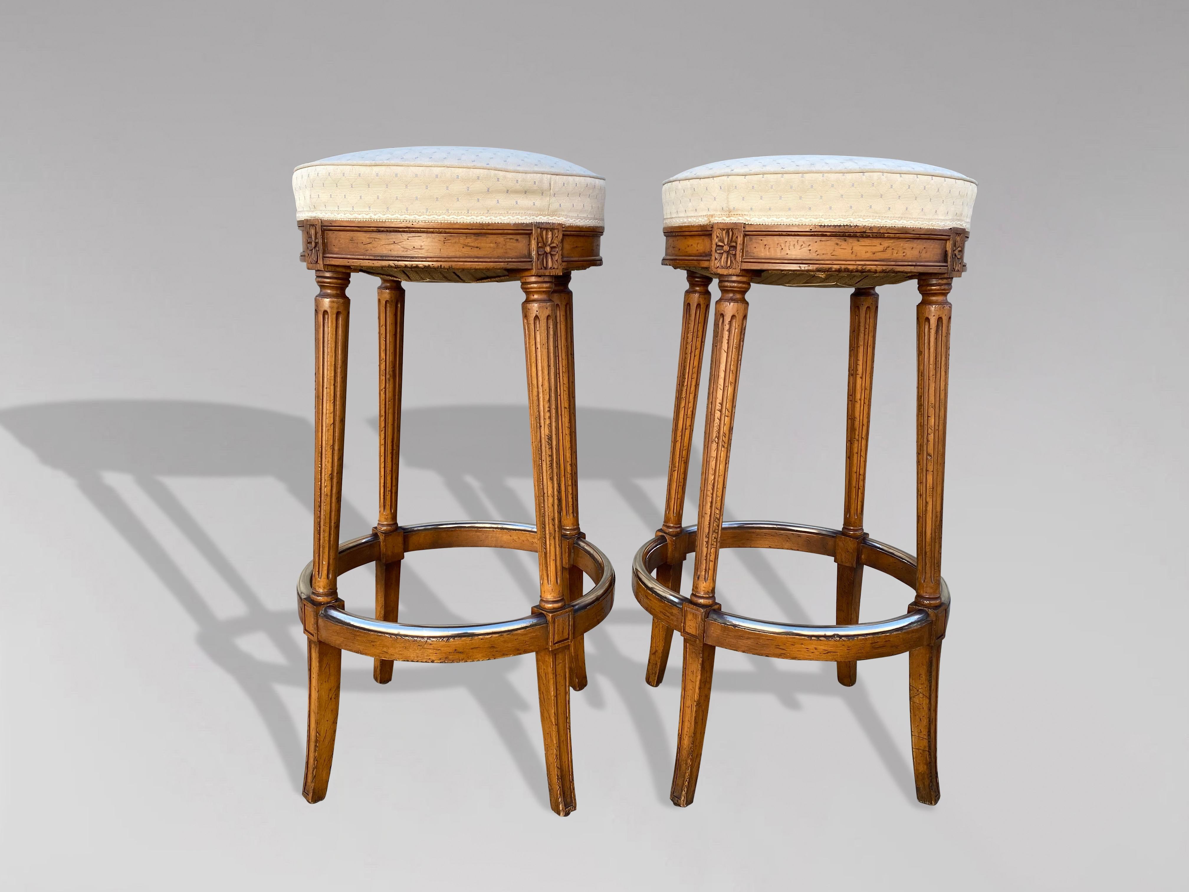 Pair of 20th century French walnut bistro bar stools or kitchen counter stools. The round seats have been reupholstered in a good quality fabric. The seats are round and are sitting on top of a solid walnut frame with splayed and hand turned reeded