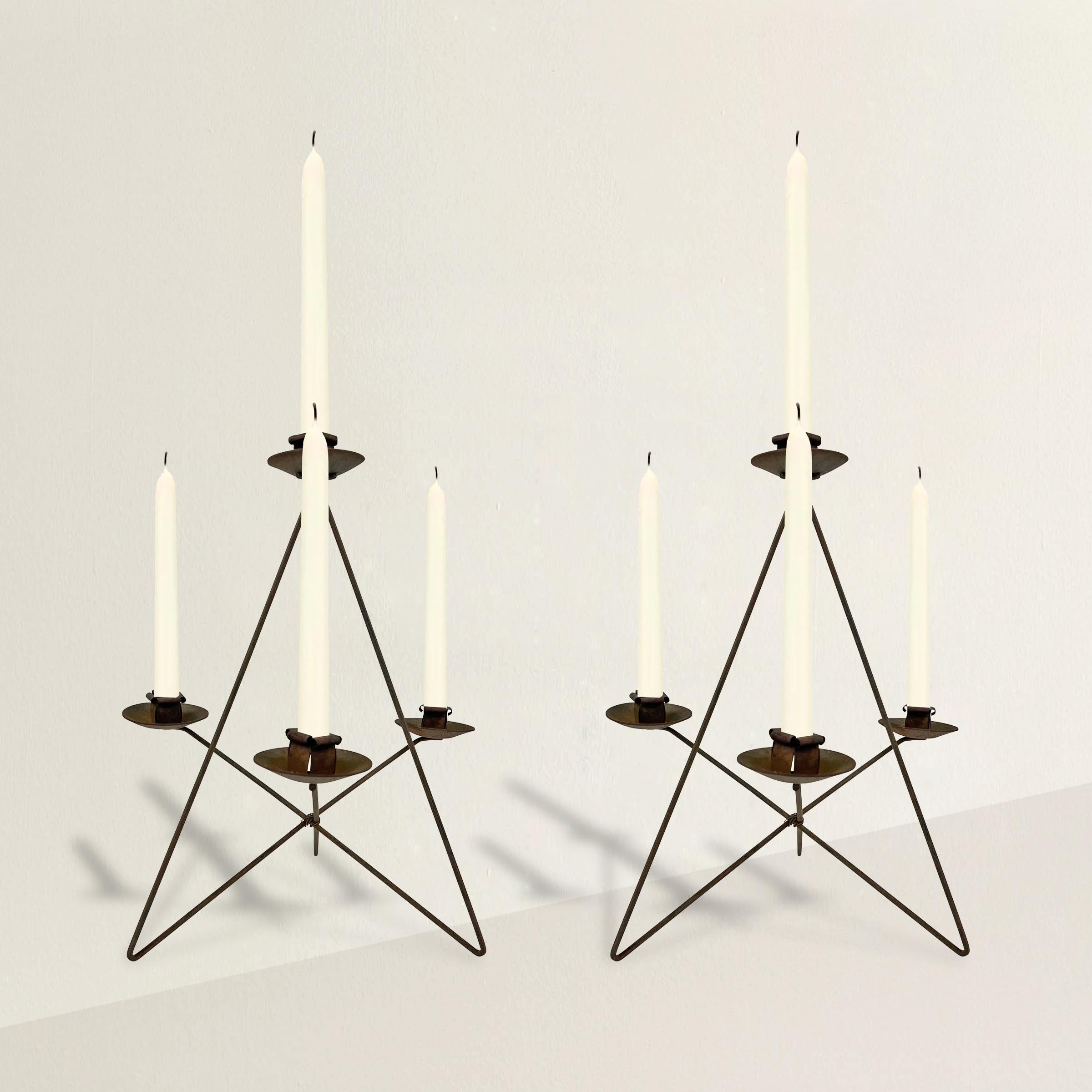 A bold pair of mid-20th century American hand-crafted iron candlesticks of pyramidal form, and each with three arms and a candle cup at the top.