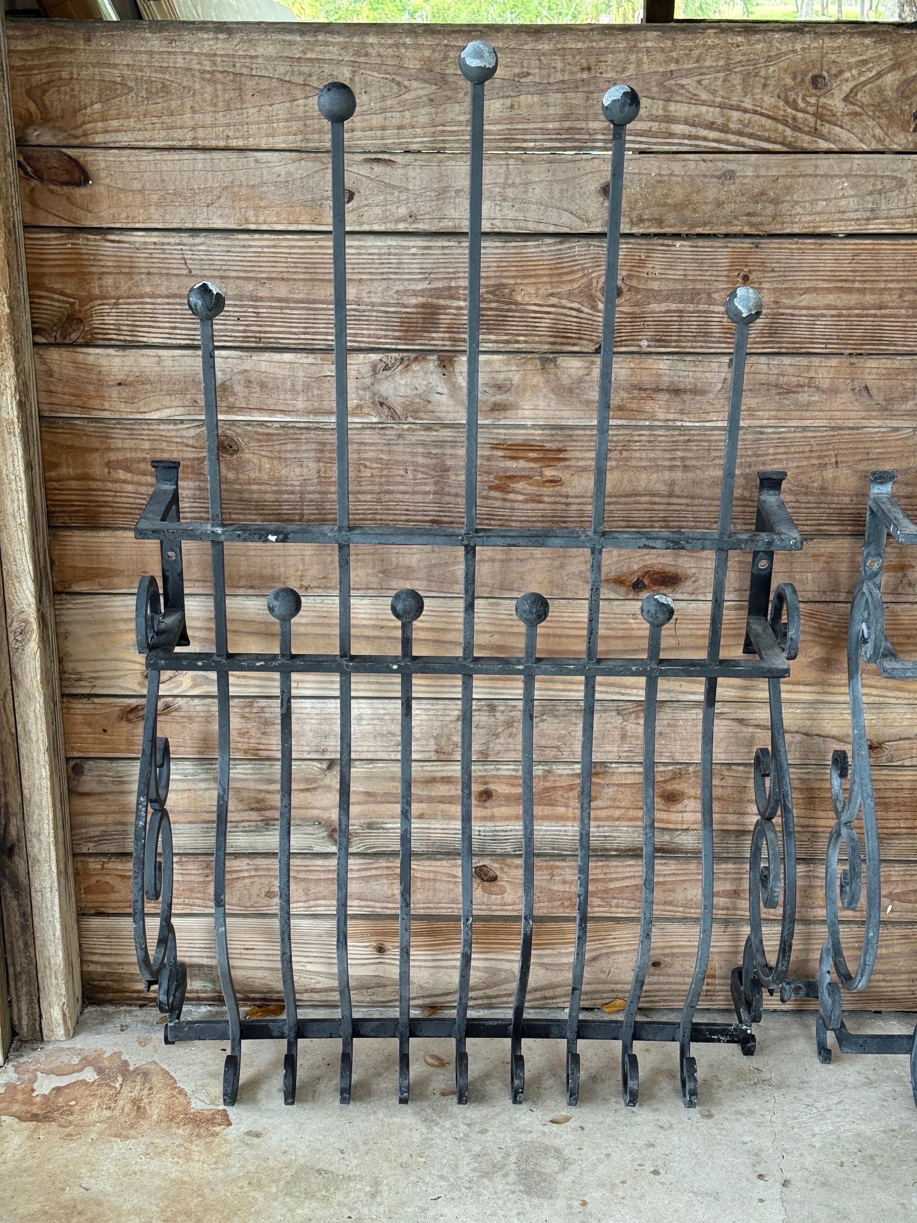 A Striking pair of Mid-20th Century hand-forged iron window grilles featuring beautifully curved lines and ornamental scrollwork.
Each piece showcases vertical rods with rounded finials and a sculptural silhouette that curves outward for