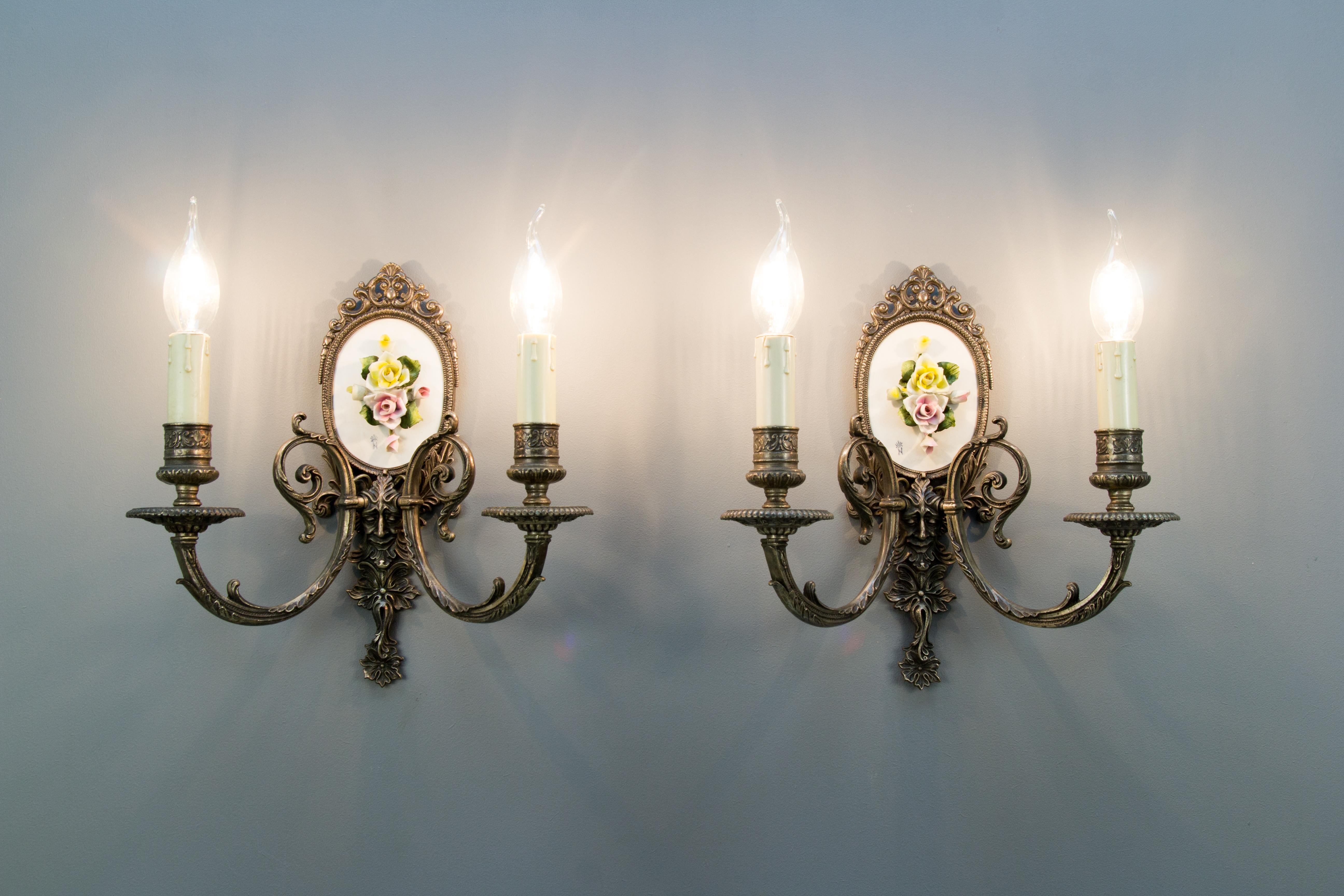 Beautiful Italian sconces decorated with Capodimonte porcelain flowers and finely made brass decors - Bacchus heads – in the center of each sconce; each sconce featuring two arms with sockets for E 14 light bulbs. Marked with the blue Capodimonte