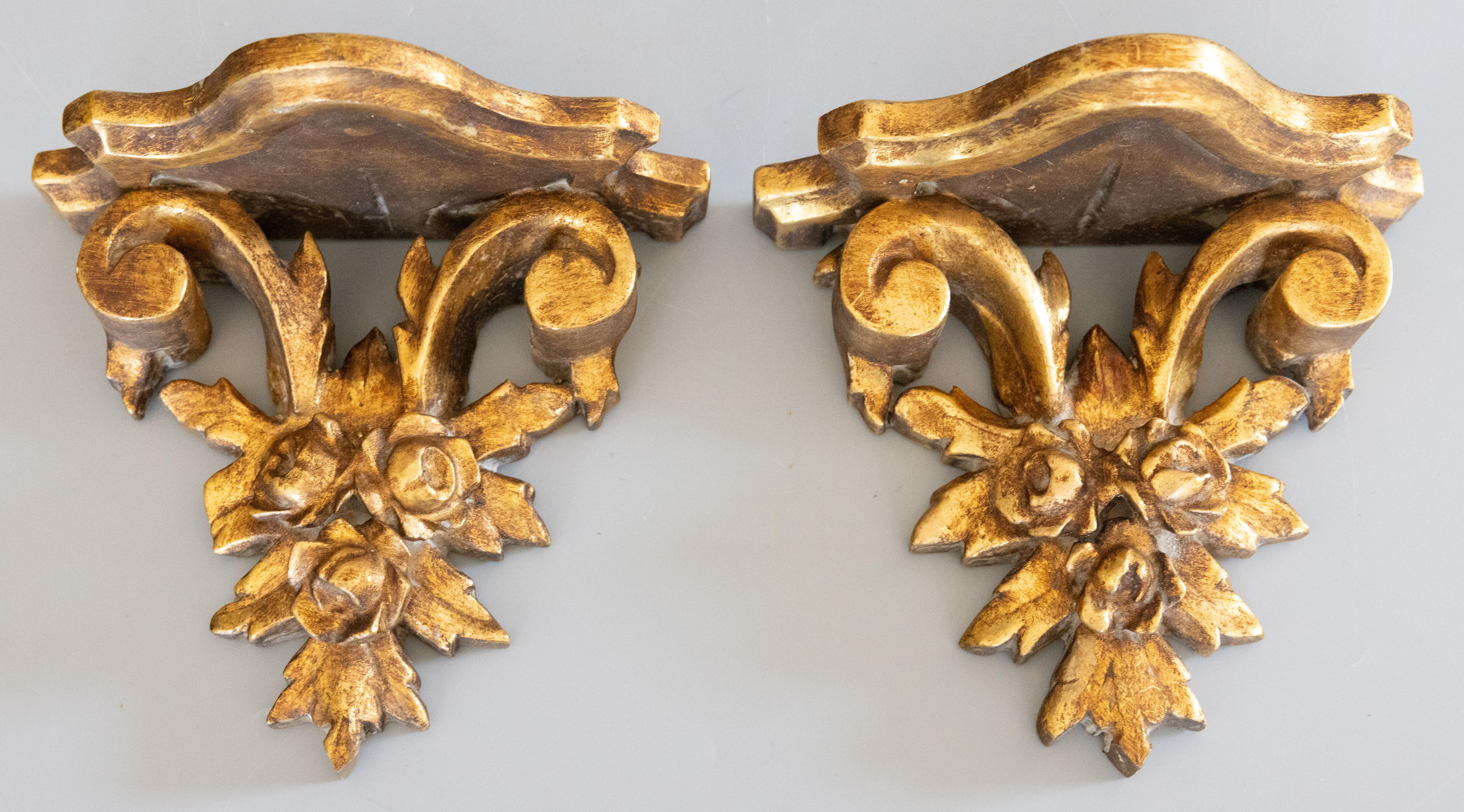 A lovely pair of vintage Italian gilded wood and gesso wall brackets shelves, circa 1950. They are decorated with lovely roses and scrolls in a beautiful gilt patina, perfect for displaying decorative collectibles or fabulous on their