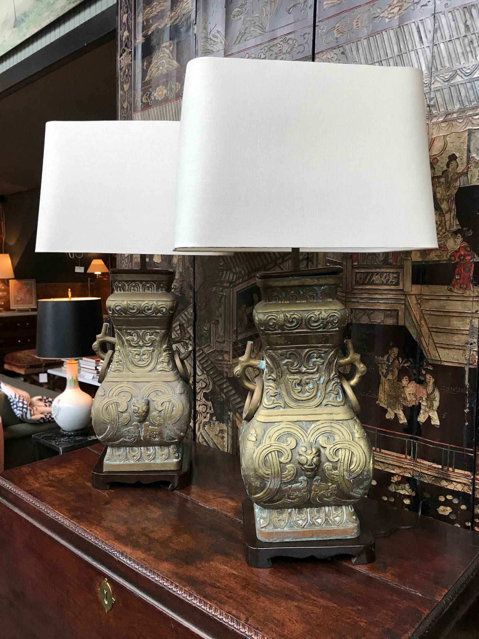 A remarkable pair of large brass table lamps in the manner of James Mont. Manufactured circa 1940s-1950s. Like Mont's creations, these lamps bring together various stylistic movements in their design. They are comprised of cast brass embossed with