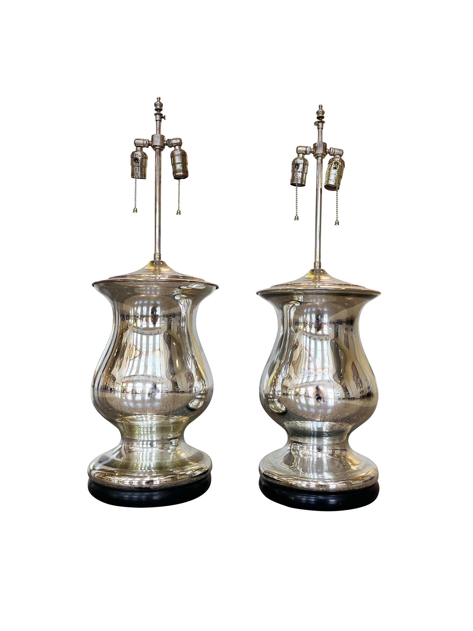 A pair of urn-shaped table lamps consisting of mercury glass bodies mounted on black lacquered wood bases. Mid-20th Century. The lamps are newly rewired with double sockets and paired with new white silk shades.

Dimensions:
33.5 in. overall