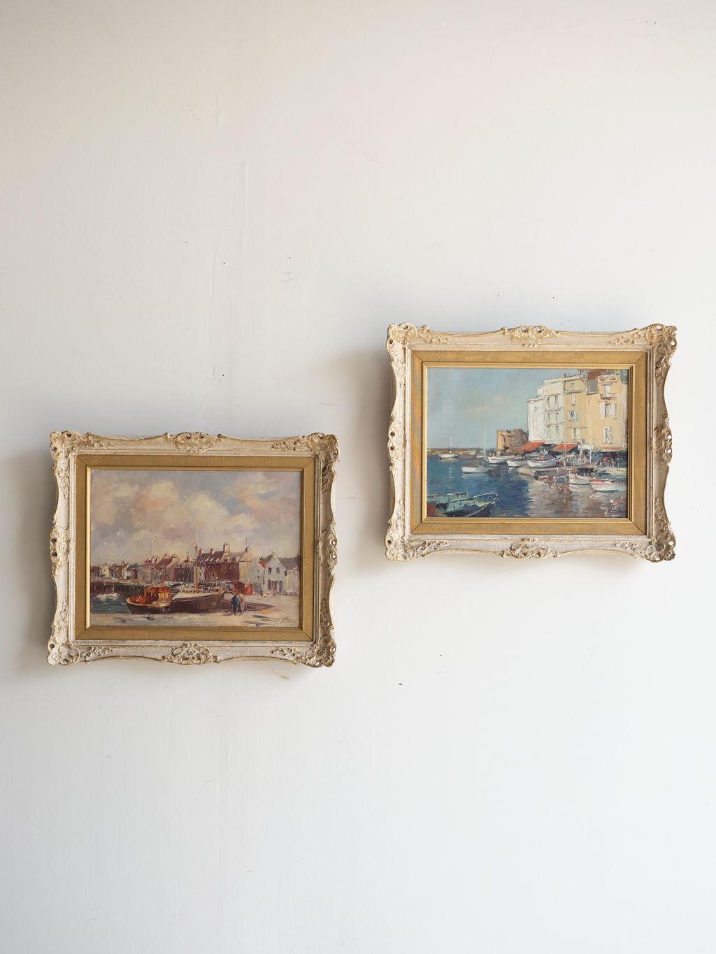 This pair of oil paintings by Phyllis Morgans features the harbors of St. Tropez and Anstruther in the mid 20th century. The dominant colors are blues and tans. The paintings are in their original frames which are a lovely gold and cream color with