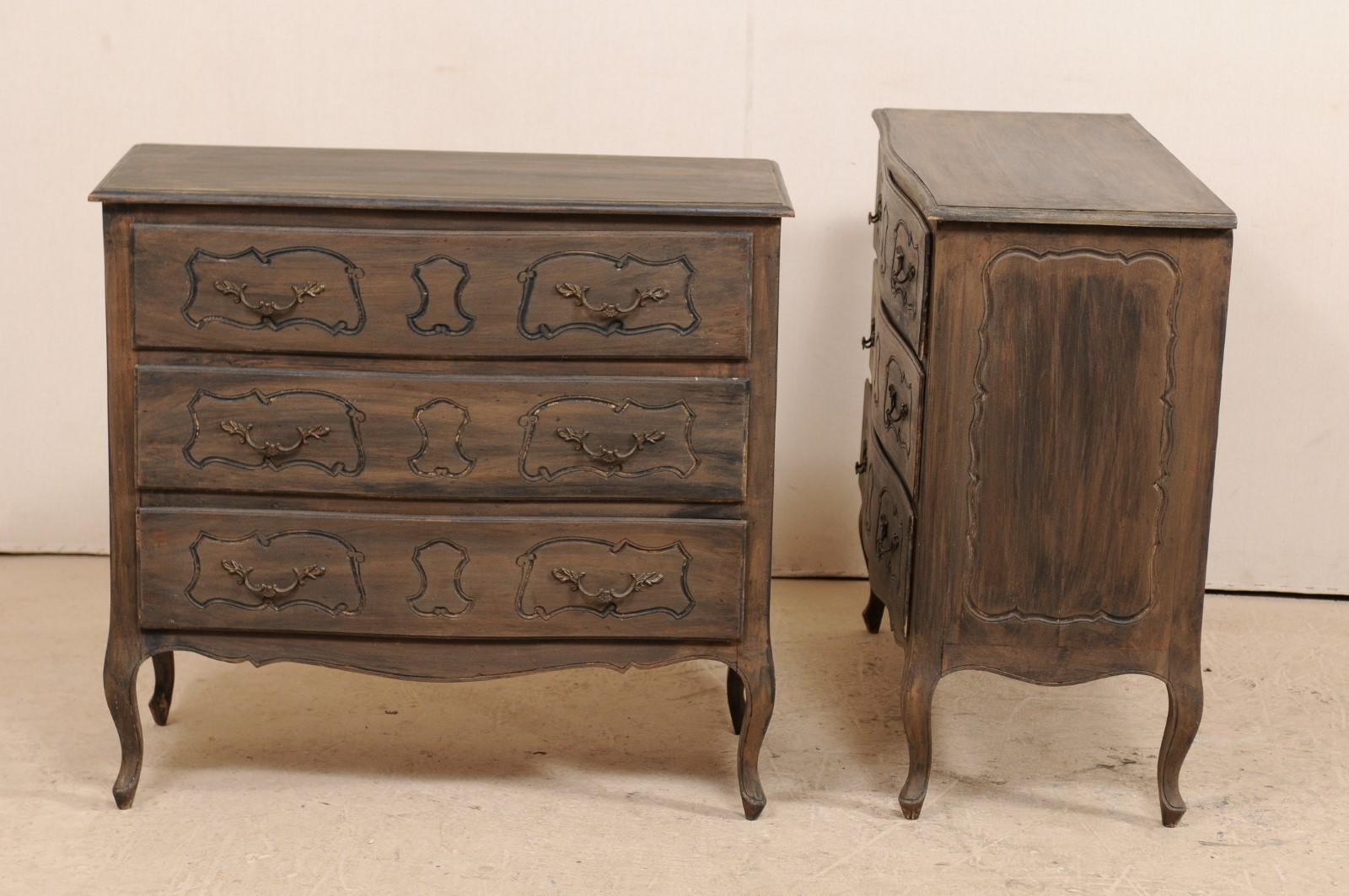 A pair of American three-drawer chests from the mid-20th century. This pair of French style painted wood chests each feature a softly bowed front, three full length drawers, each with molded panels with carved cartouches at center, decoratively