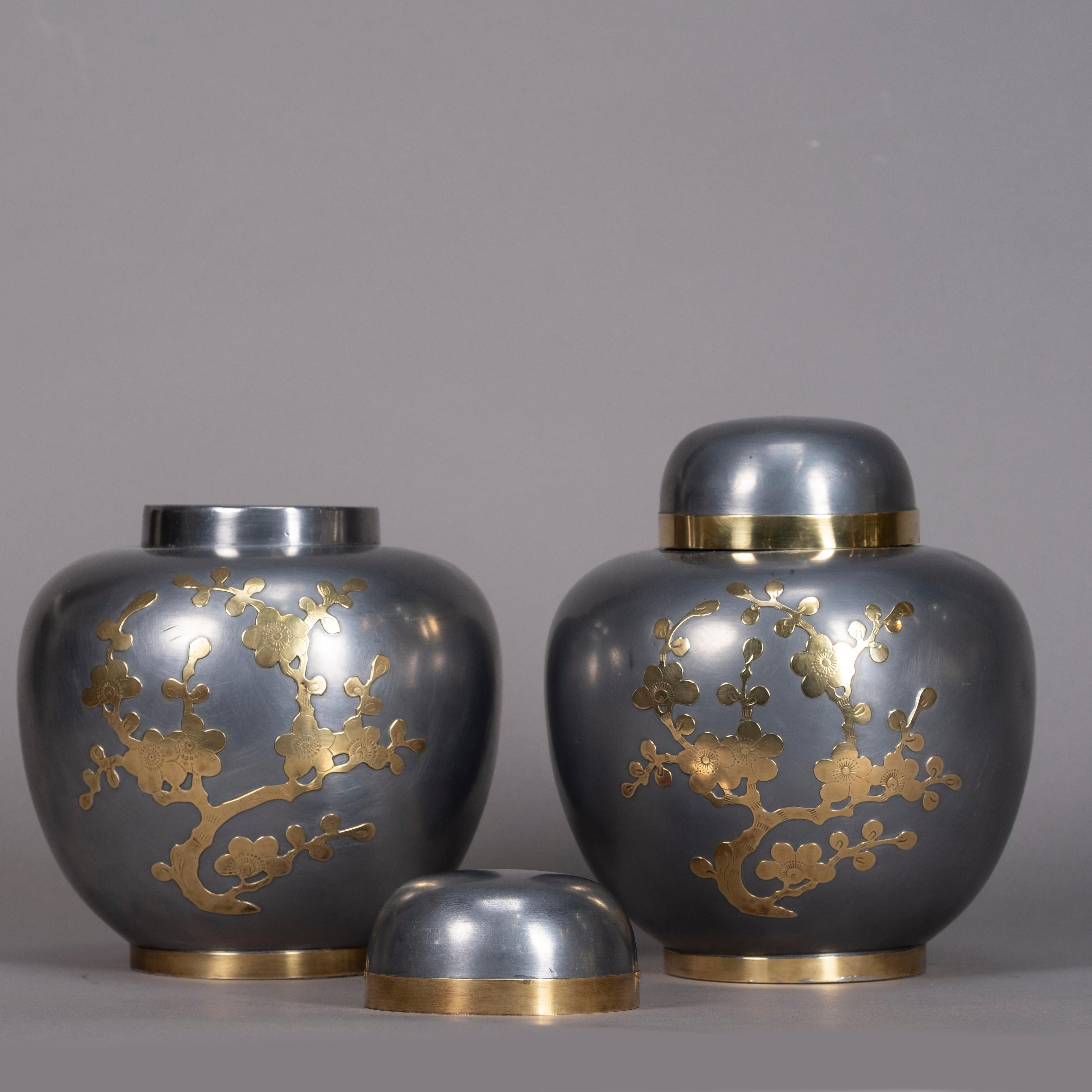 A pair of polished pewter ginger jars and covers, of bulbous form, the bodies inlaid with brass cherry blossom.