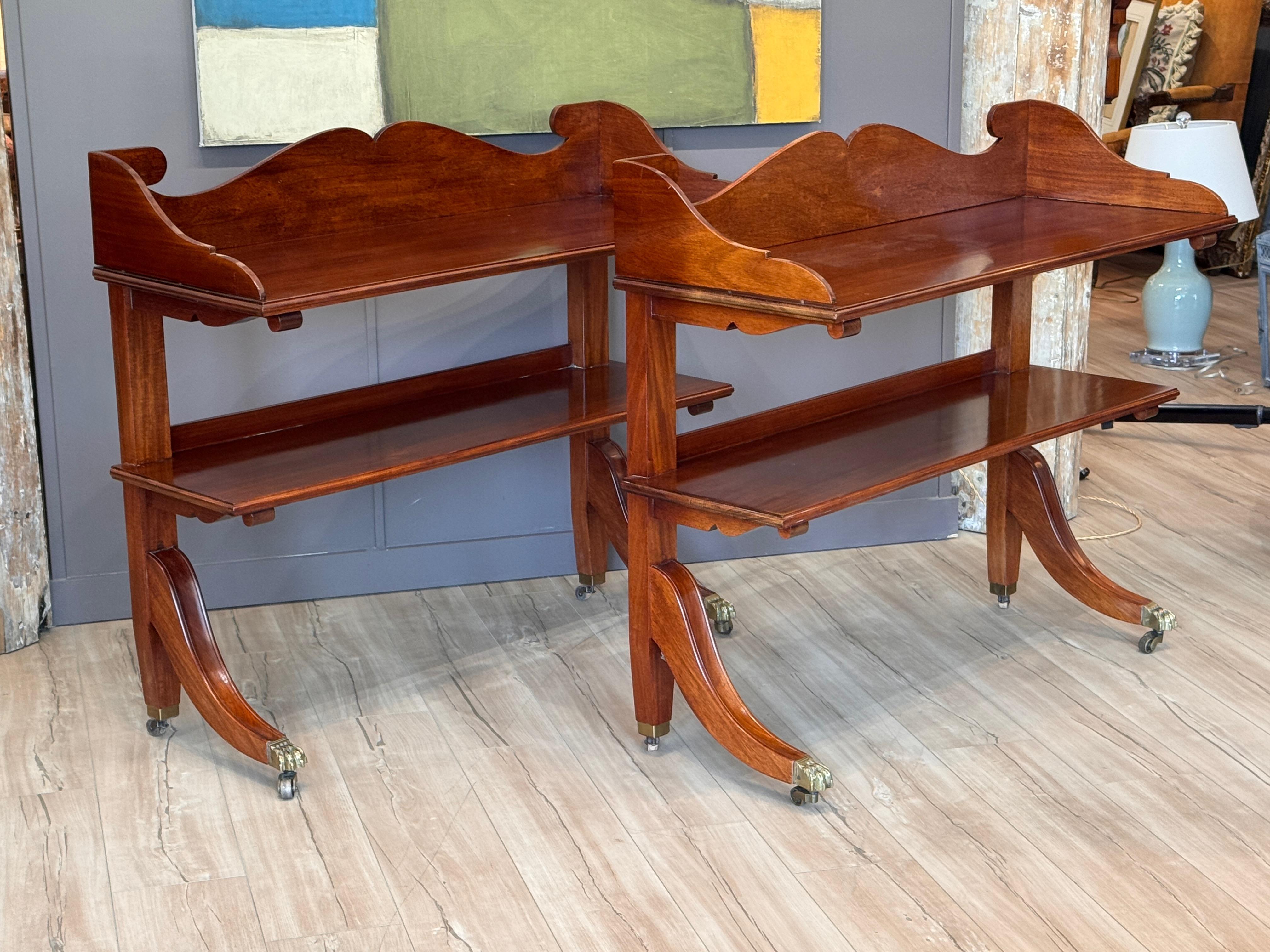 Coppia di étagères a due ripiani in mogano in stile Regency della metà del XX secolo con gambe strombate che terminano con piedi a zampa e rotelle in ottone. Il design enfatizza le linee pulite e le proporzioni classiche, con una falegnameria
