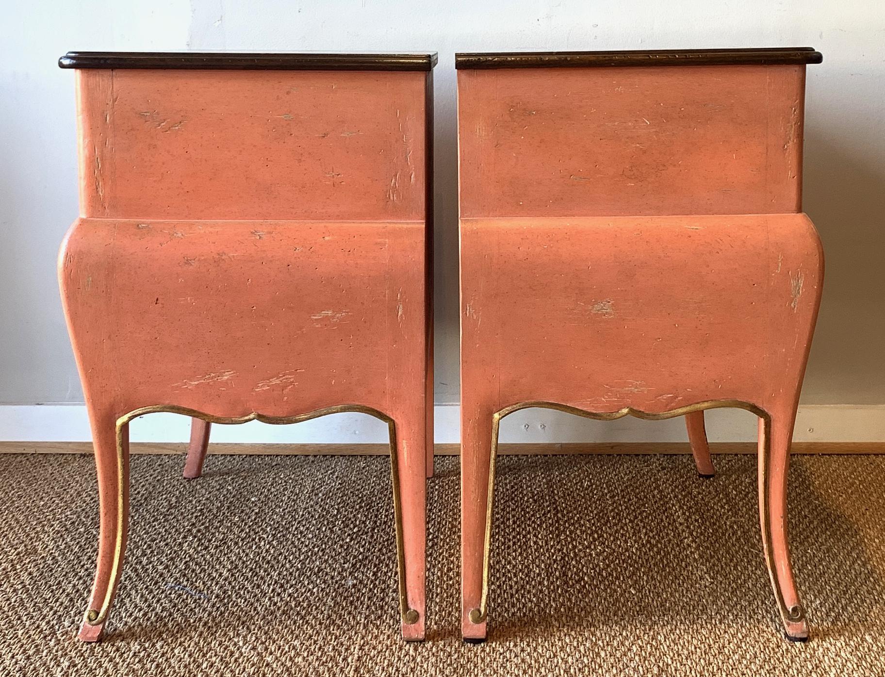 An elegant pair of mid-20th century. salmon colored two-drawer bombé side or night tables with gilt decoration made by the New York manufacturer, Auffray & Co.
