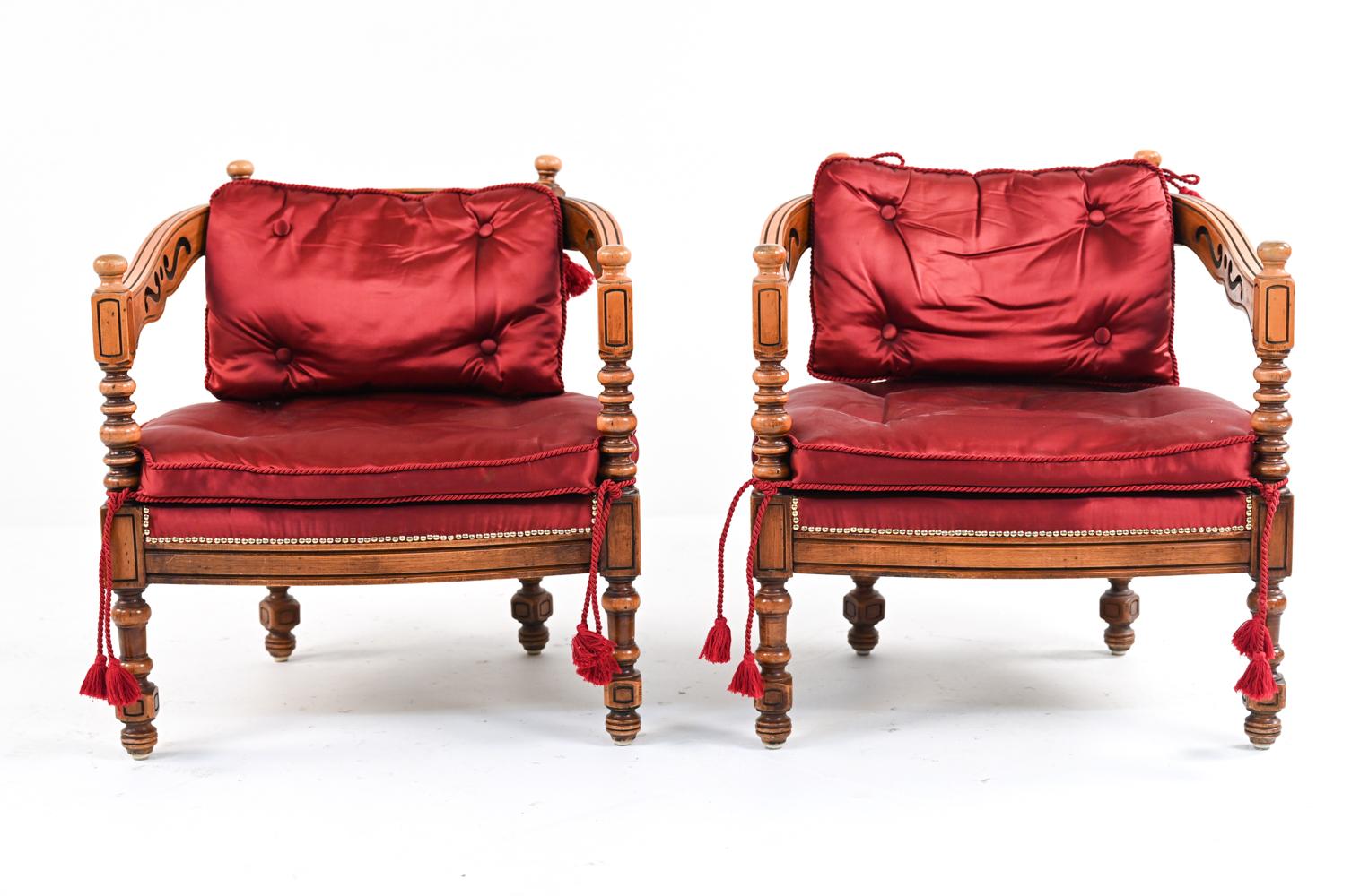 Add flair to your living space with this highly unique pair of Mediterranean Gothic Revival armchairs, featuring open carving, polished brass nailhead trim, and dramatic burgundy satin upholstery with corded tassels. Circa Early- to Mid-20th Century.