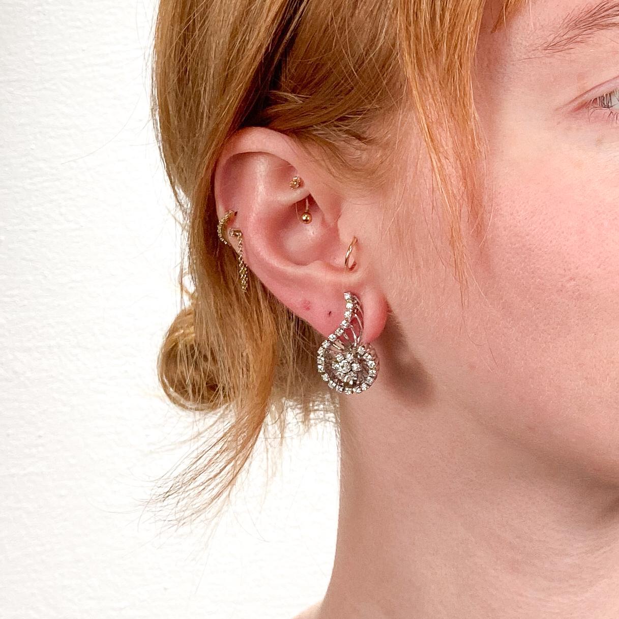 Un bel paio di orecchini di diamanti retrò.

In oro bianco 18 carati.

Con una forma a spirale o a punto interrogativo che circonda un centro a grappolo stilizzato a forma di fiore e con diamanti bianchi taglio rotondo incastonati.

Con un totale di