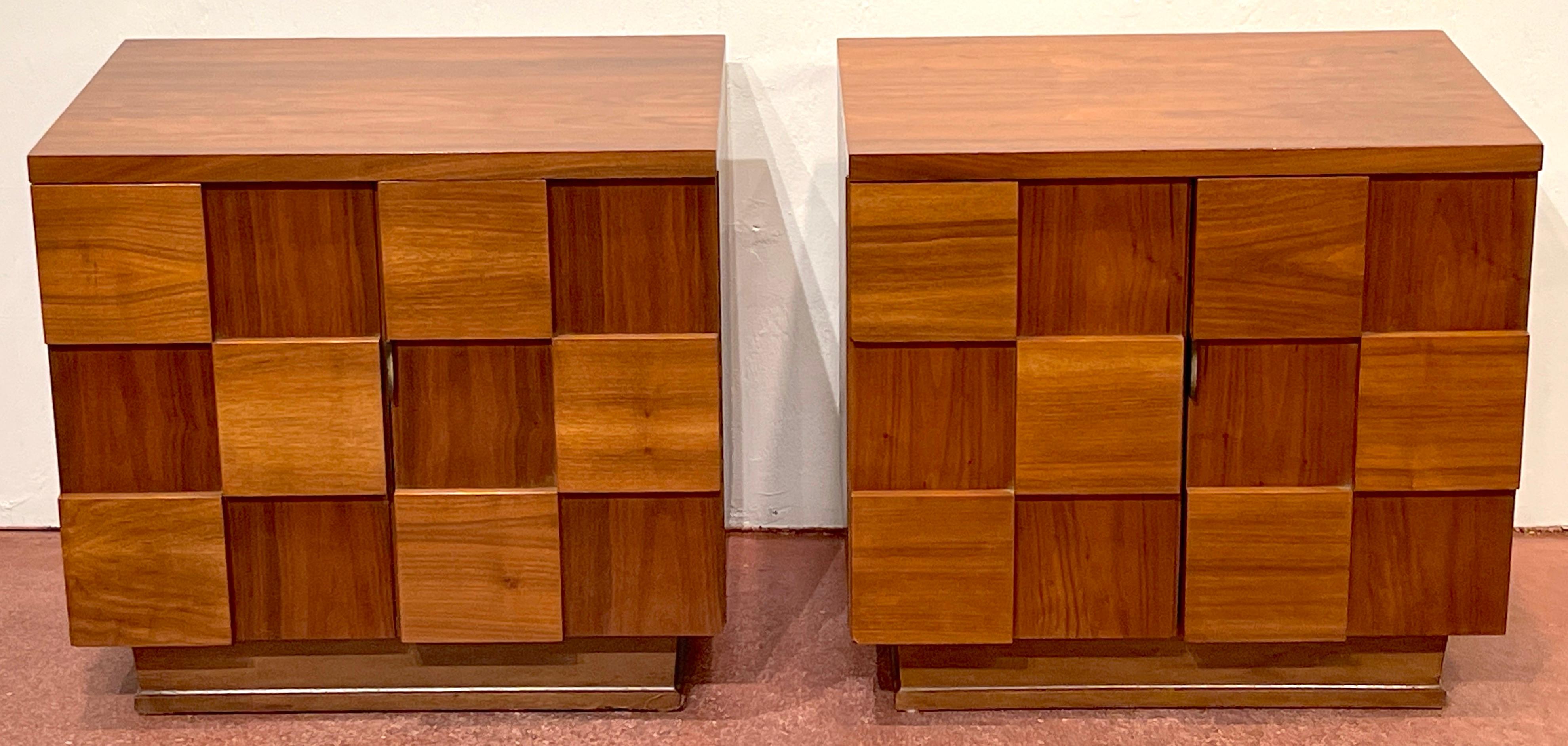 Pair of mid-century American designer walnut 'Checkerboard' nightstands.
USA, Circa 1970s

Each one of rectangular form, fitted with two raised sculptural swing-doors with 24 raised and lower walnut cubes, with brass handle, revealing a generous