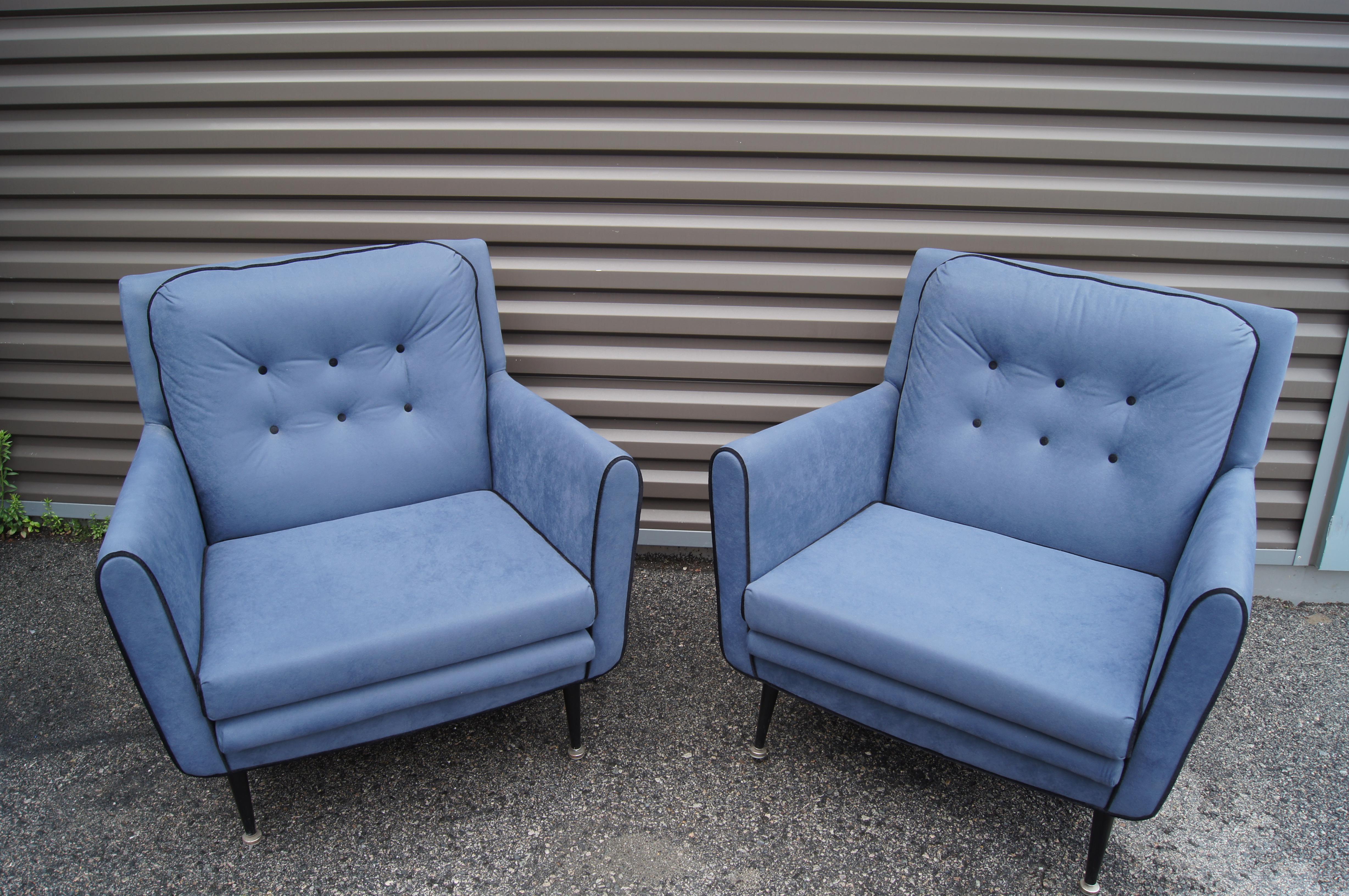 This pair of handsome lounge chairs features a distinctly American 1950s silhouette with tapered black metal legs and a tufted back cushion. The capacious frames have been reupholstered in a soft blue microfiber with contrasting black piping.