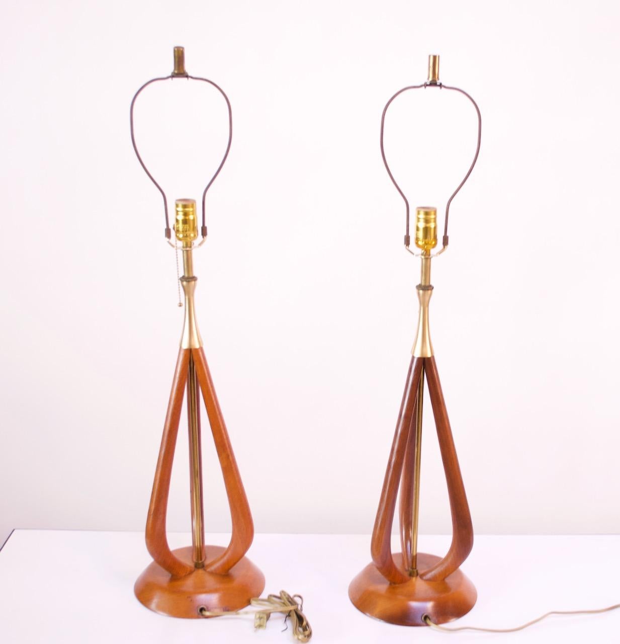 Sculptural pair of 1950s American Modern table lamps composed of a round, solid walnut platform base and carved frame that houses a brass-plated rod at the center. Lamps are finished on the top by gold brushed-aluminum mounts connected to brass
