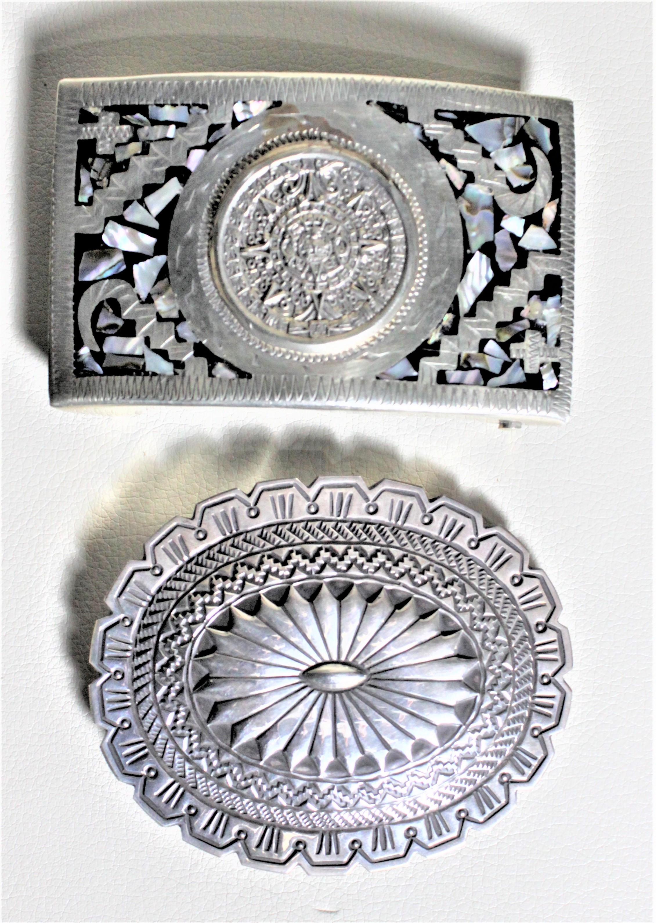 This pair of midcentury silver and turquoise belt buckles are presumed to have been made in circa 1965. The buckle with the round central medallion and inlaid with mother of pearl is believed to be Mexican. The oval shaped buckle is artist signed by