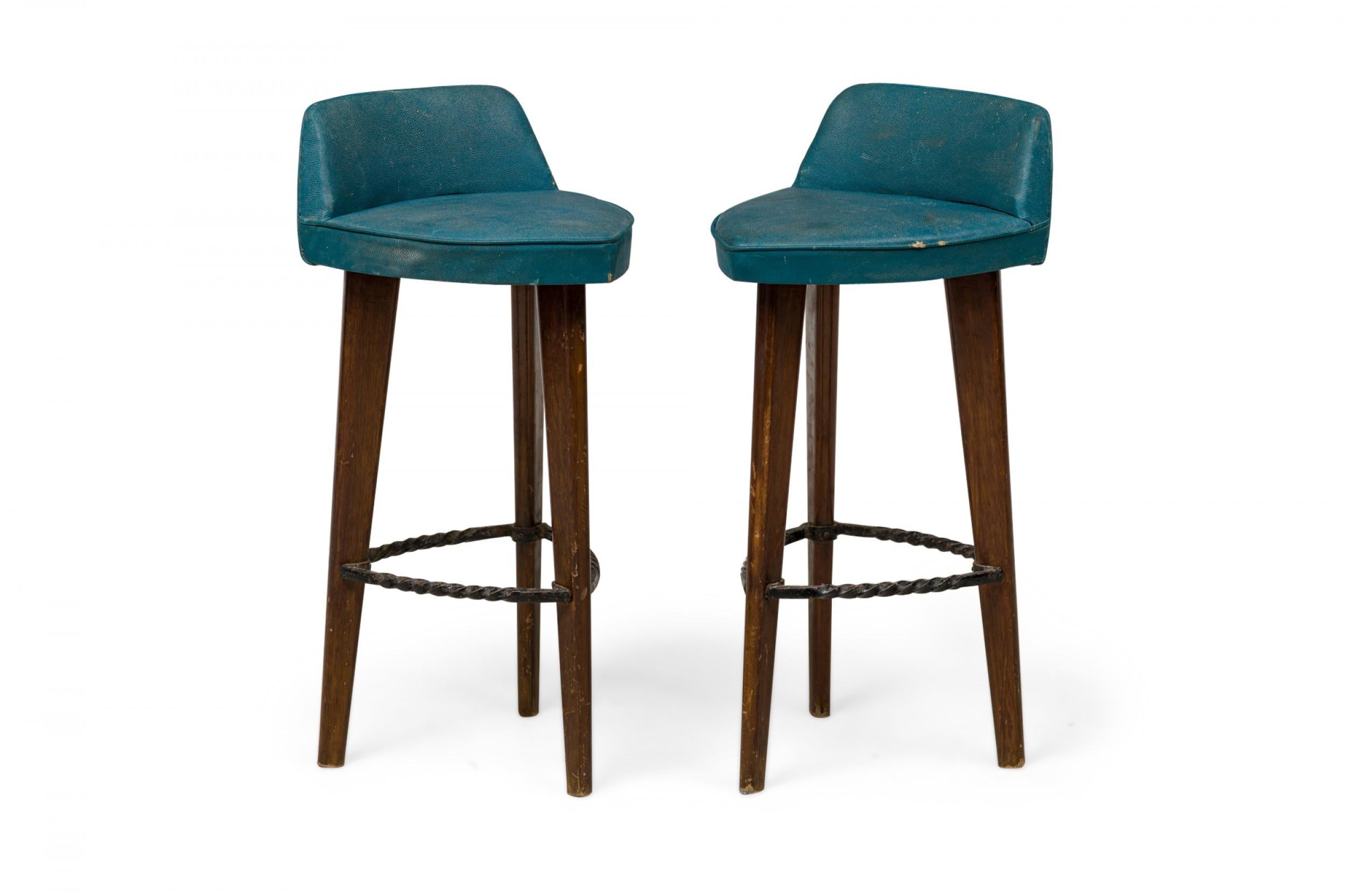 Pair of Mid-Century American triangular blue vinyl upholstered bar stools with low backrests, a splayed tripod wood frame and metal twist foot supports.

Wear and losses.