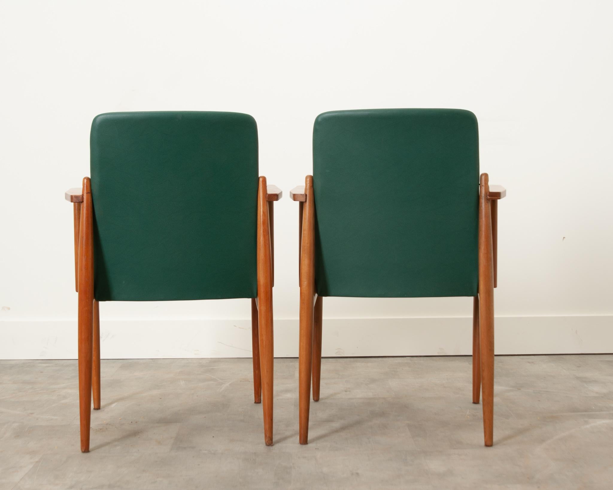 A stylish pair of Mid-Century Modern armchairs from 1960’s France. Chair slates are upholstered with green vinyl and a sleek frame crafted from fruitwood; these are the perfect way to add a pop of color to any living space. The seat height is 17-½”