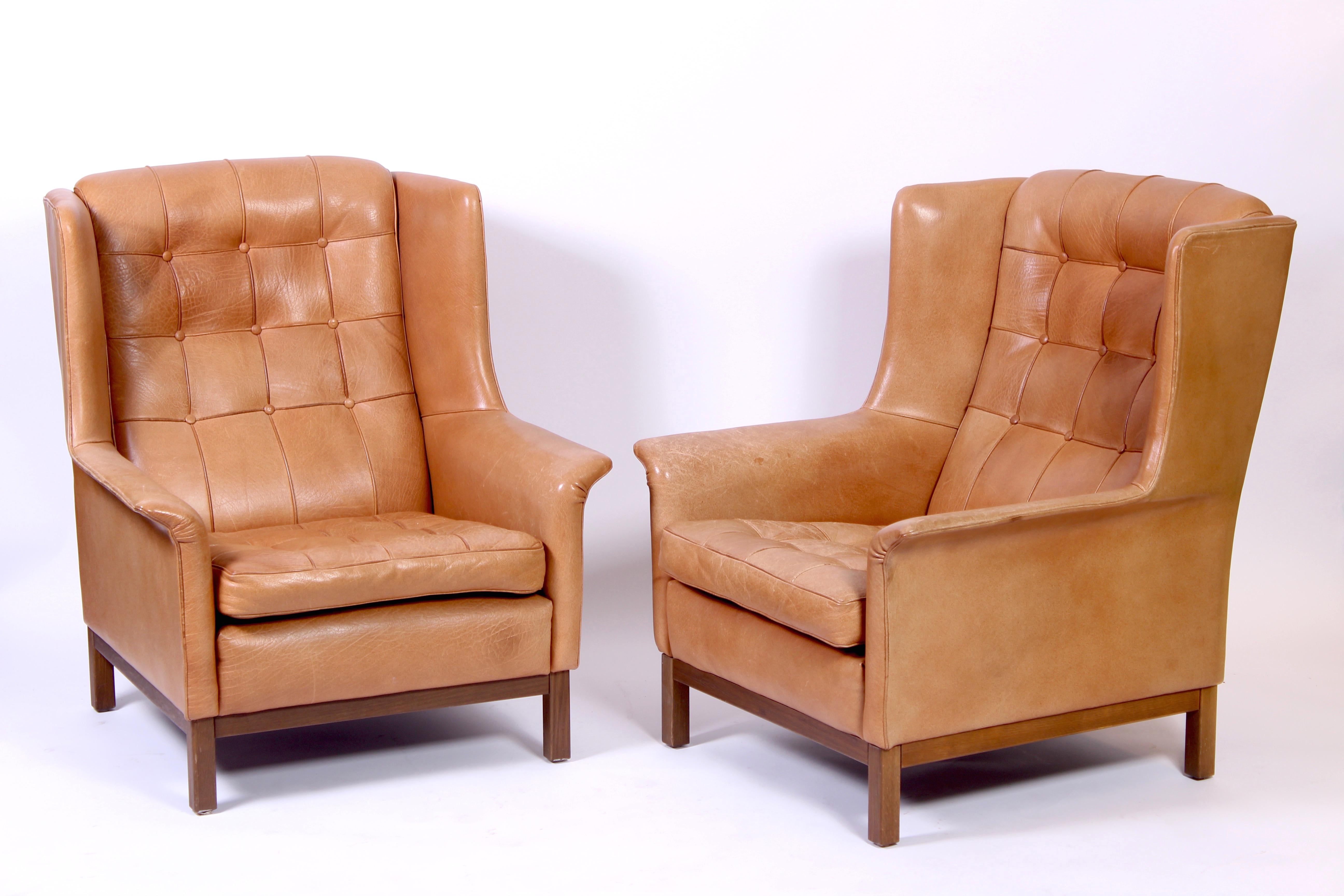 A pair of high quality midcentury lounge chairs by Swedish designer Arne Norell. The chairs has original thick buffalo leather with nice patina. The set also includes one ottoman on wheels that has the same patina.
Very good vintage condition with