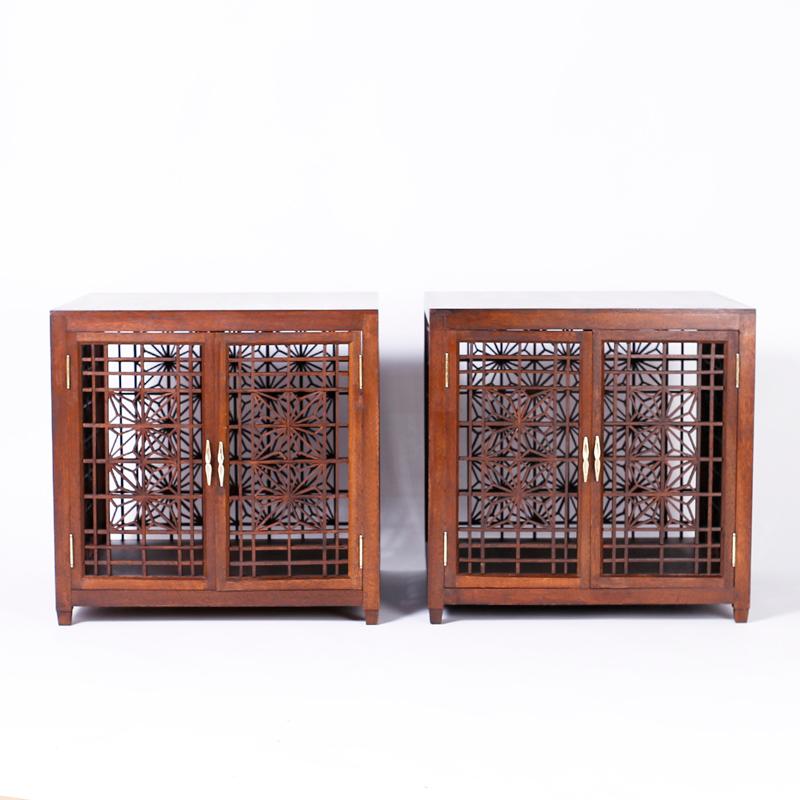 Pair of Asian Modern two-door stands or cabinets crafted in mahogany, with unusual fretwork doors, backs and ends, in the chinoiserie manner.