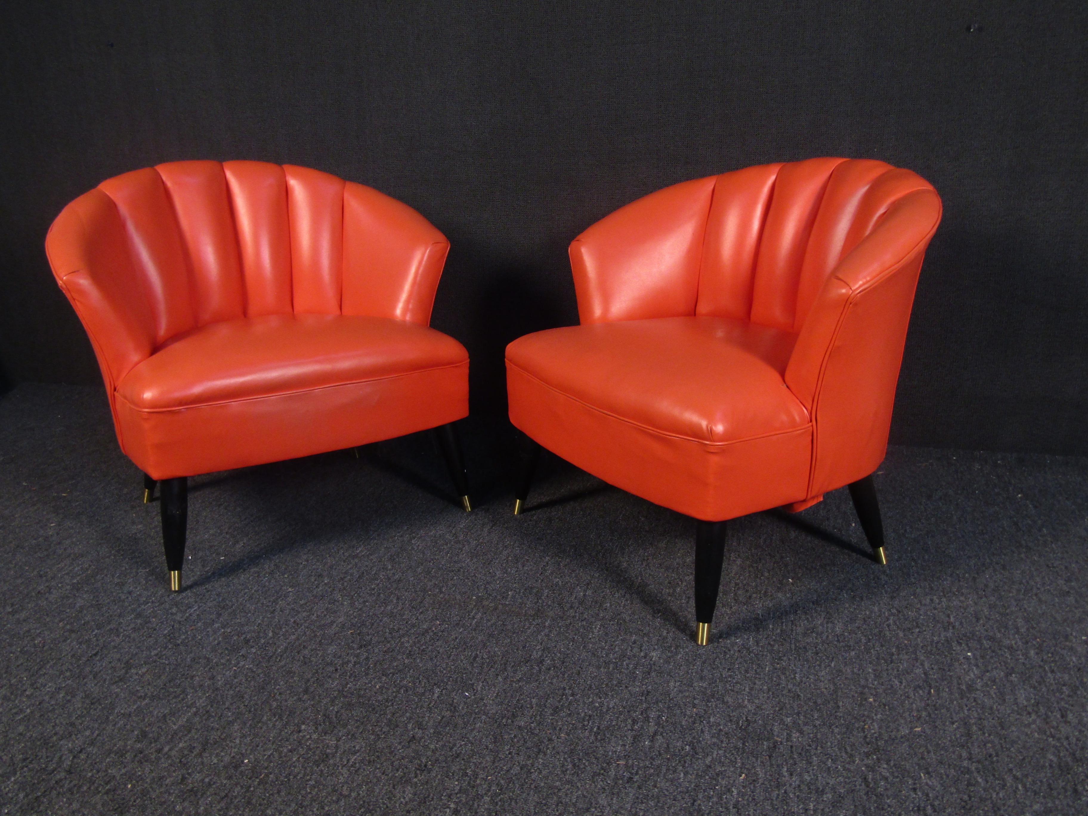 A stunning pair of midcentury style club chairs. This sleek and comfortable pair rests on tapered wooden legs. An oyster-shell design with elegant coral Naugahyde makes these perfect for any setting. This stunning pair of contemporary lounge chairs
