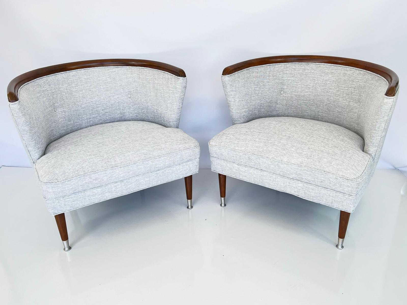 Zwei mit blauem/grauem Leinen gepolsterte Bergersessel im Stil der Jahrhundertmitte. Jeder wannenförmige Stuhl hat eine geschwungene Nussbaumkrone, die die gepolsterte und getuftete Rückenlehne überragt. Ein lockeres Drop-in-Kissen sitzt auf einer