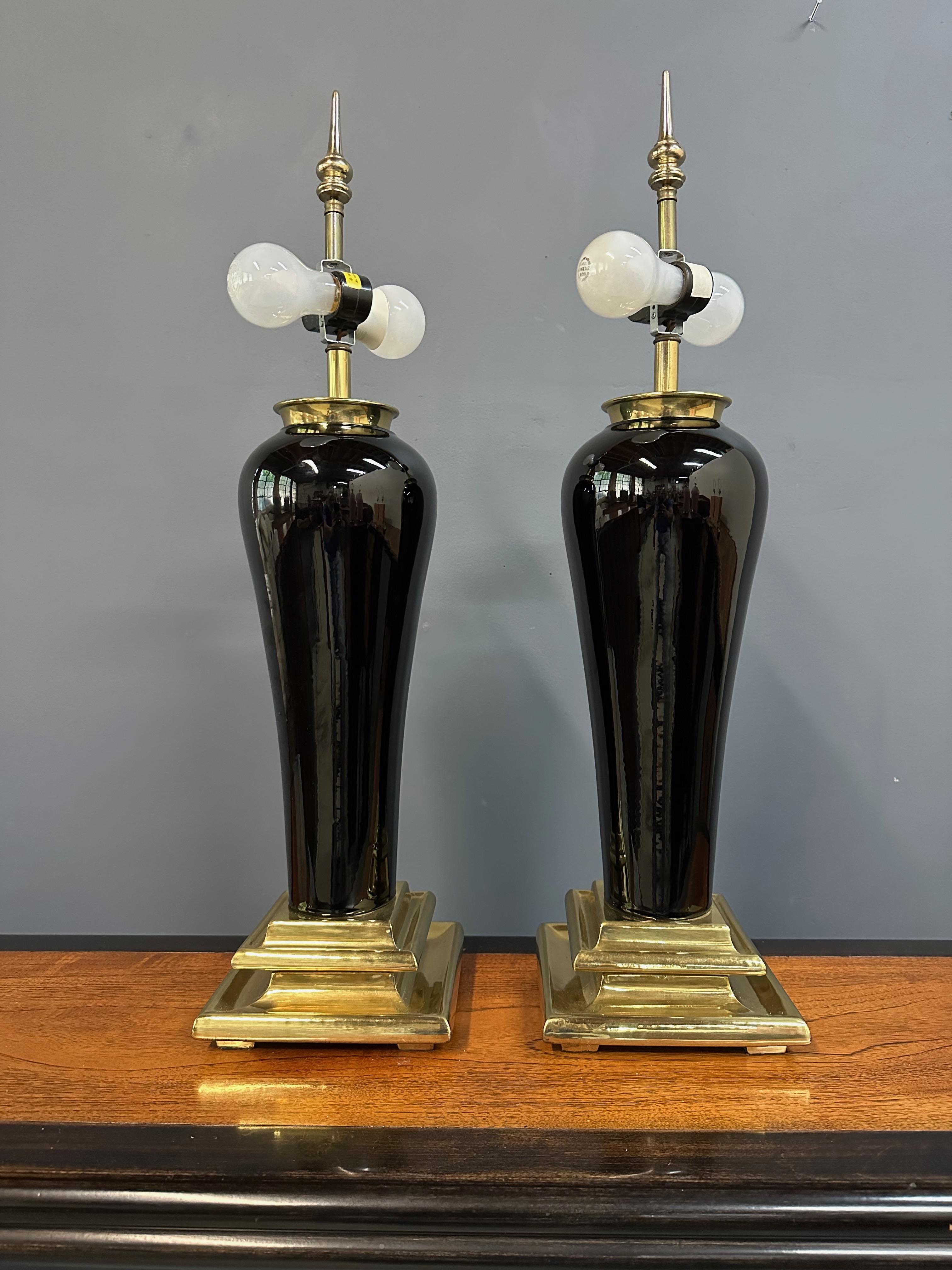 Striking and sculptural, this pair of monumental table lamps by Chapman from the 1980s showcases a bold silhouette in high-gloss black ceramic with tiered brass bases. The classical urn-shaped bodies are elevated by neoclassical stepped bases in