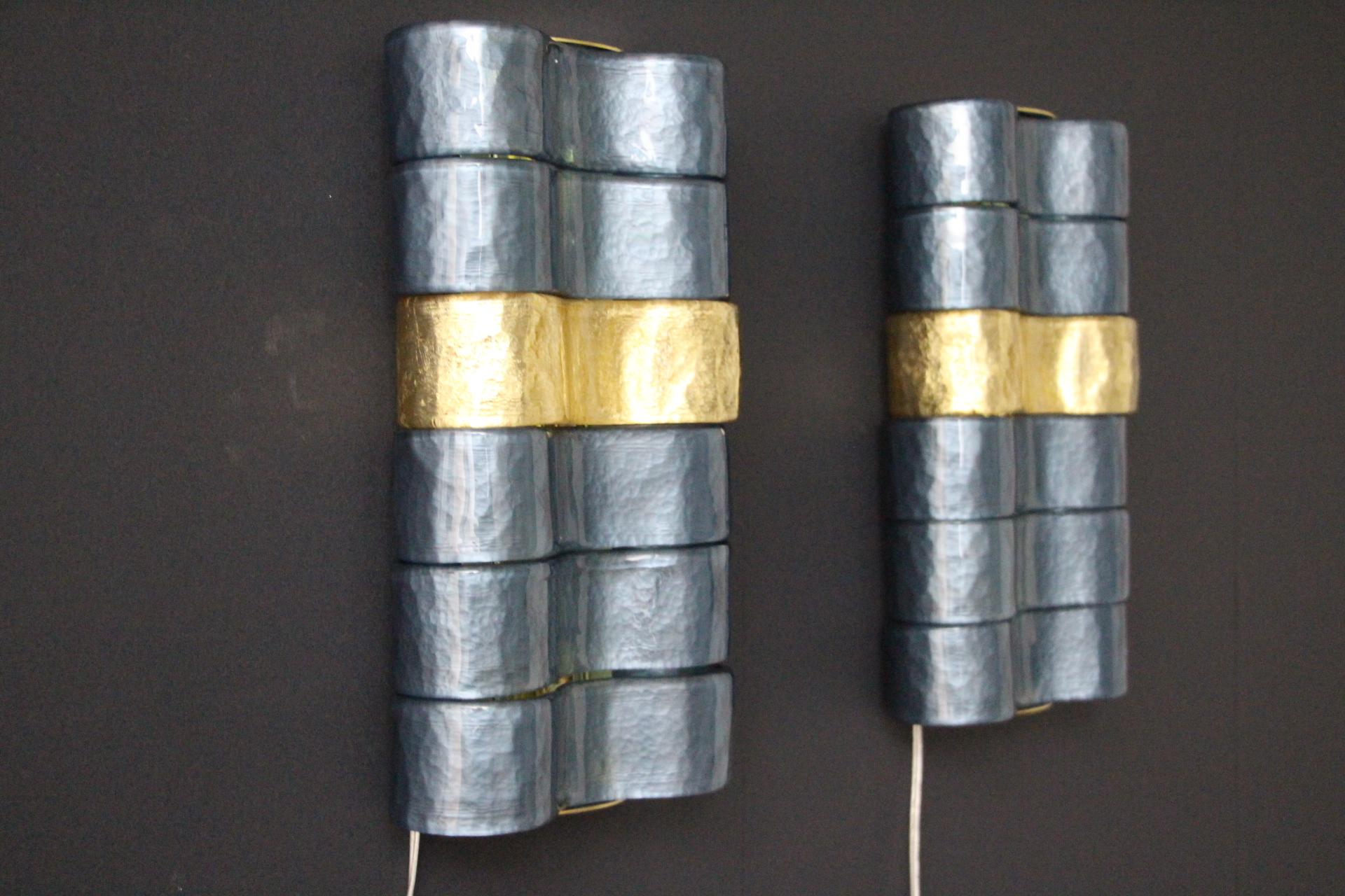 Dieses Paar von Wandleuchtern ist wunderschön. Sie ist mit großen geschwungenen Glasbändern aus blau-grau irisierendem und goldenem Glas versehen. Jedes Stück Glas wurde von Handwerkern in Murano einzeln handgefertigt. Sie bestehen aus