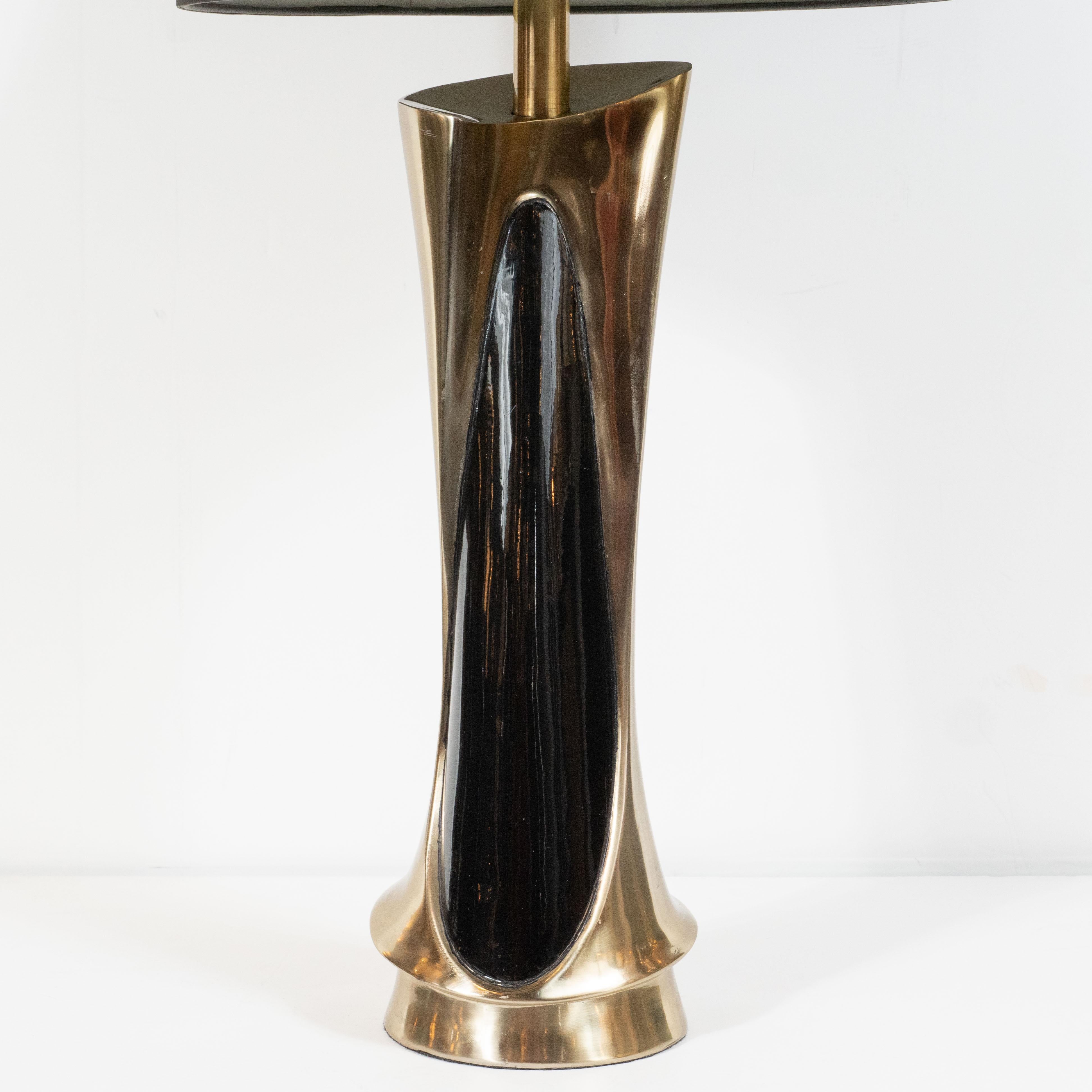 This refined pair of brutalist table lamps were realized in the United States by the Laurel Lamp Company, circa 1970. They feature circular bases and amorphic bodies with brass backs and elliptical ebonized walnut inlays, which offers a beautiful