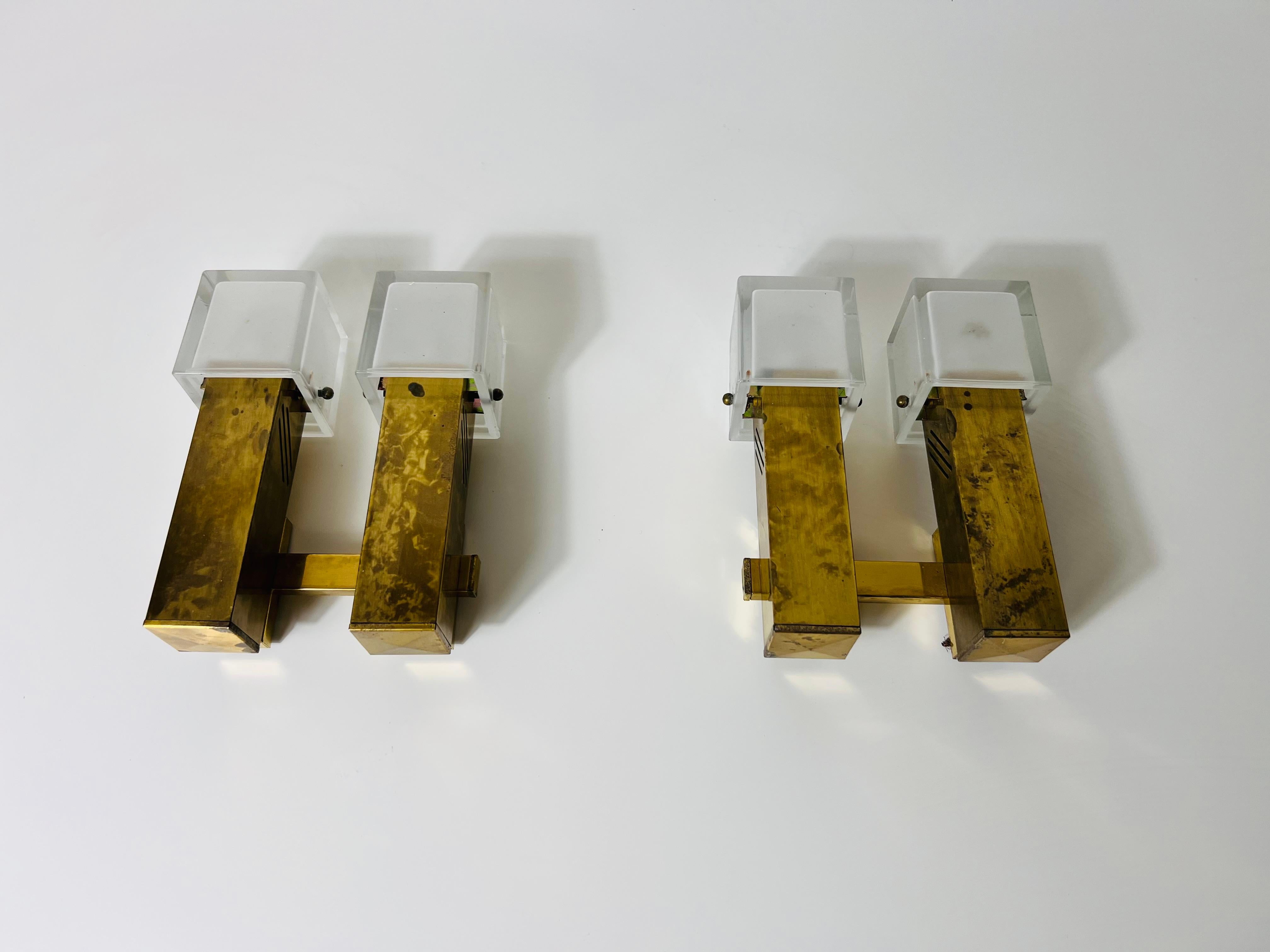 These exquisite wall lamps, crafted in Italy during the 1960s, are made entirely of solid brass, showcasing a sleek, angular design influenced by Bauhaus aesthetics. The lamps feature striking ice glass shades, which are securely fastened to the