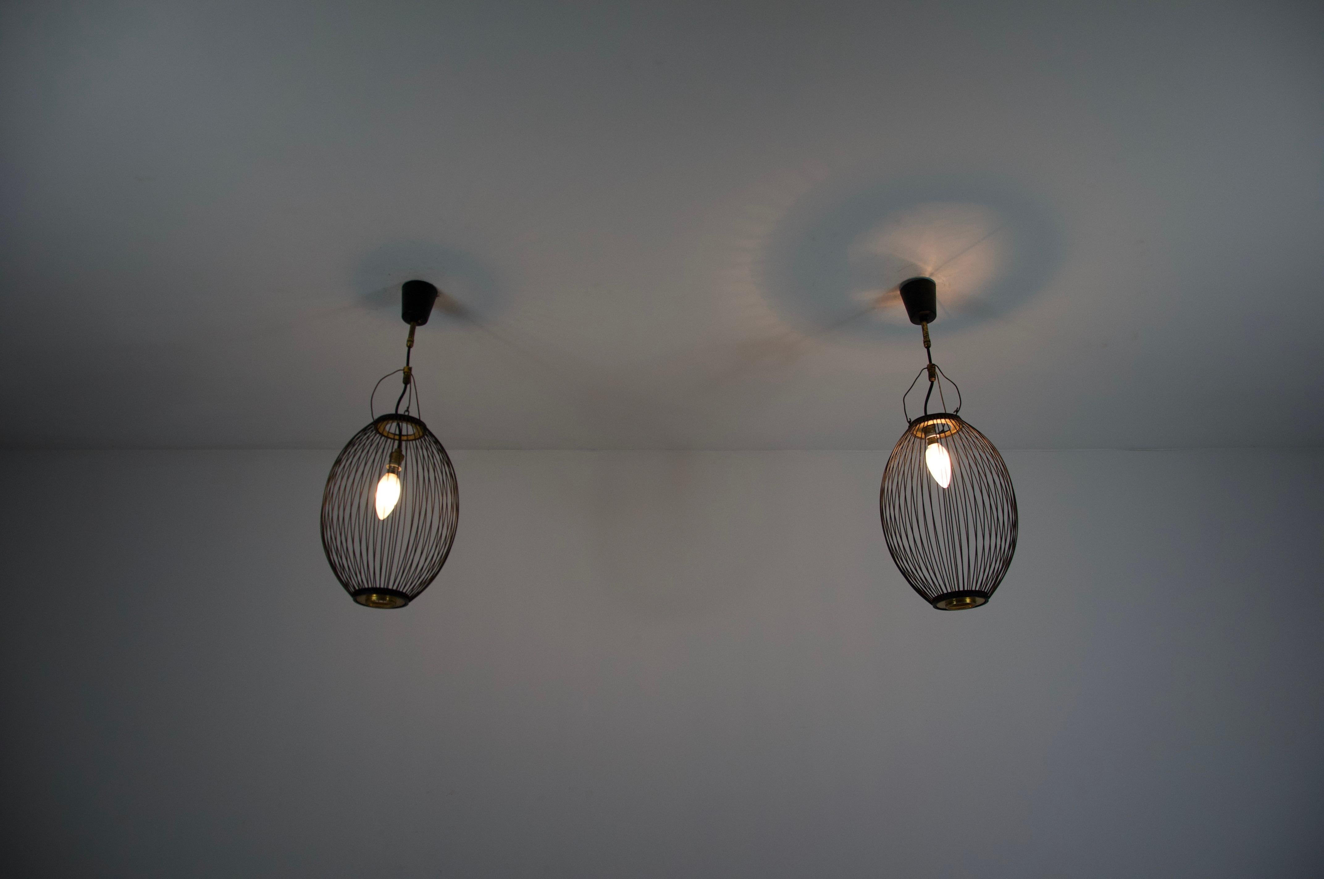 Cette paire de lampes suspendues italiennes du milieu du siècle, datant des années 1960, met en valeur le mélange raffiné de forme et de fonction de l'époque. Chaque lampe présente un design de cage allongée, de forme ovale, composé de fils