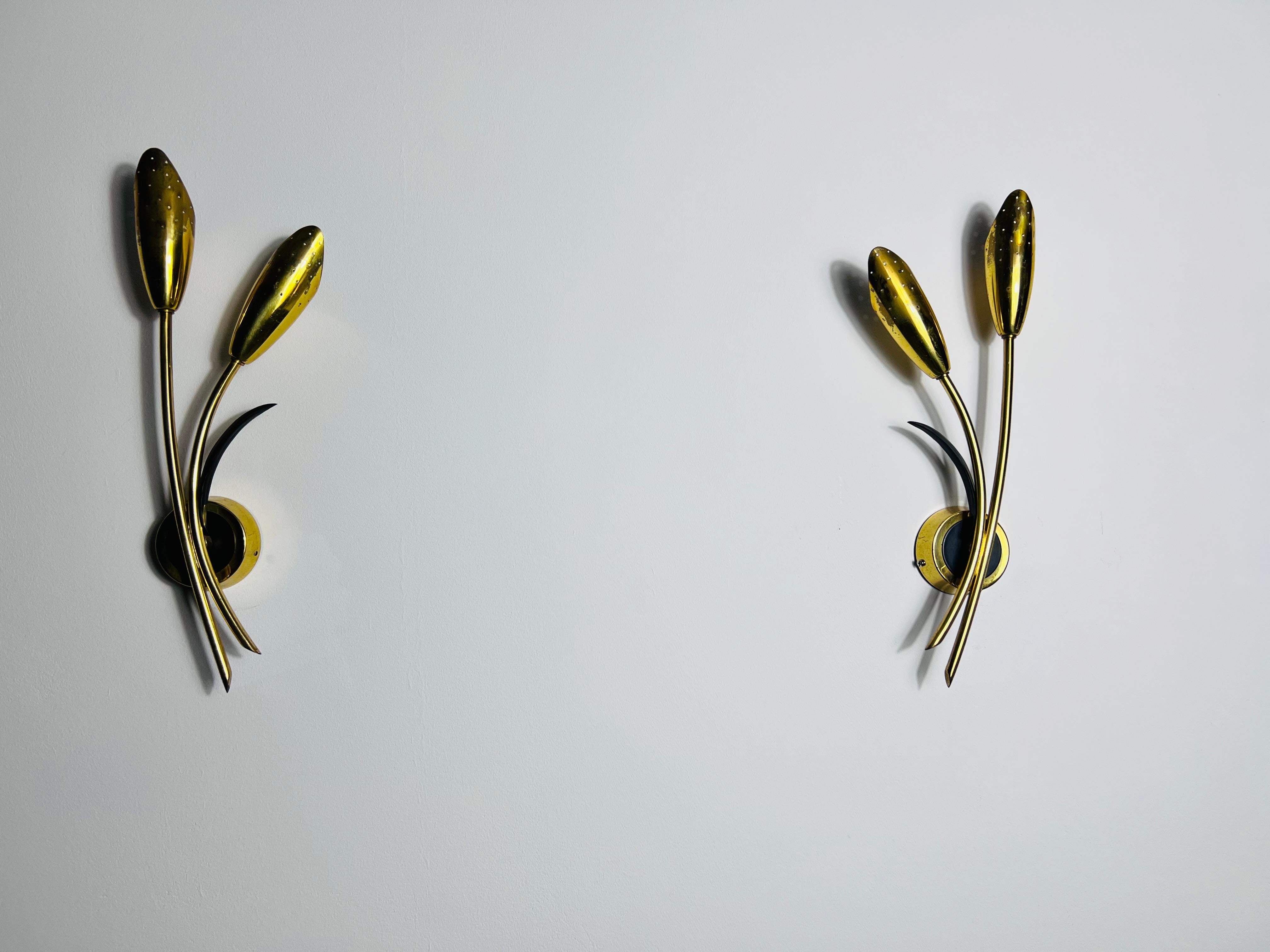 These exquisite Sputnik wall lamps from Italy, circa 1960s, are a perfect blend of mid-century modern design with a hint of floral elegance. Each lamp features a dual-headed design with two brass light heads, complemented by a black plastic rod for