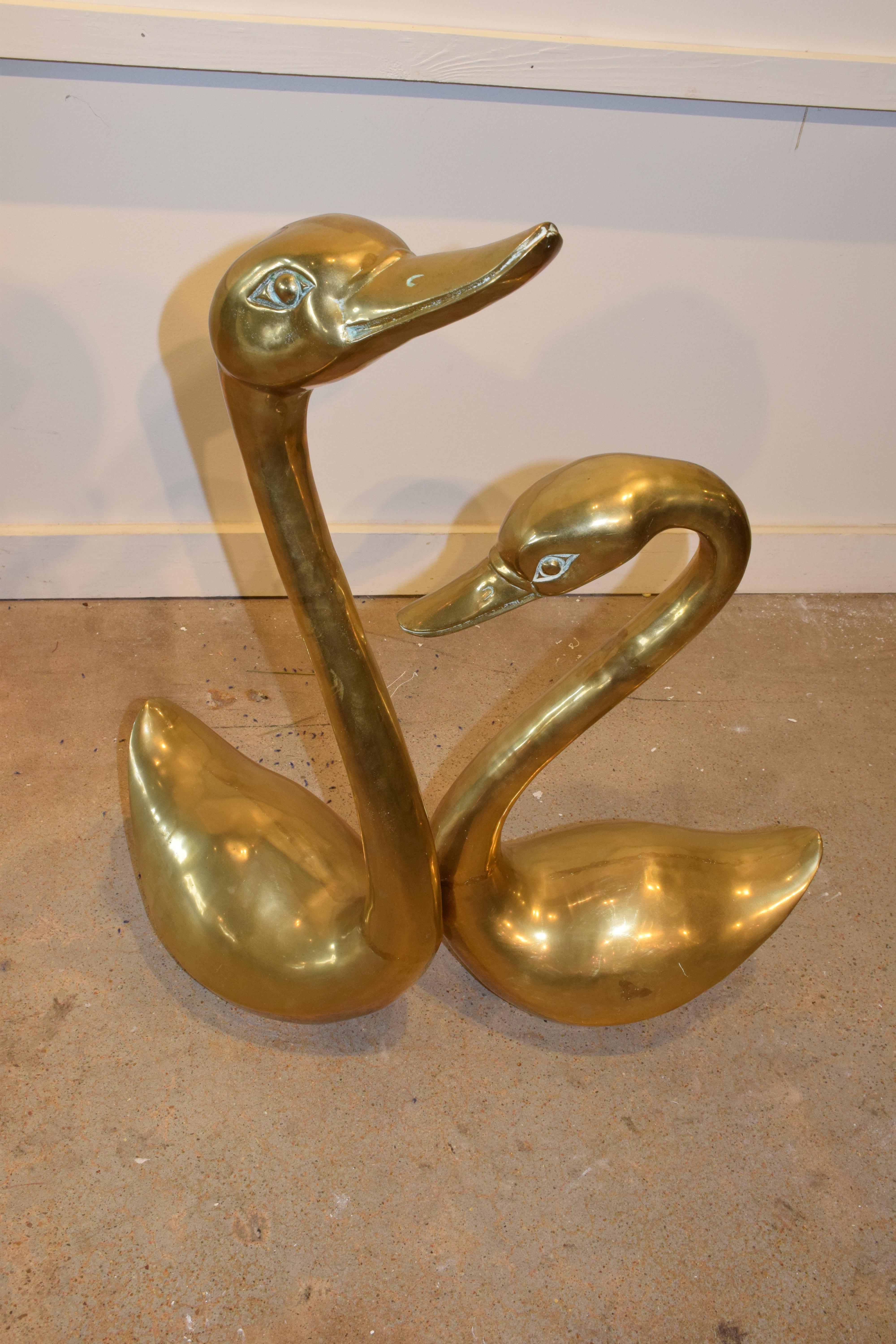 These beautiful brass midcentury swans would be a great addition to your home. This lovely pair will add a bit Mid-Century Modern used as a table centerpiece or resting on the floor. The larger swan measures 29 inches high, 13.5 inches wide and 8