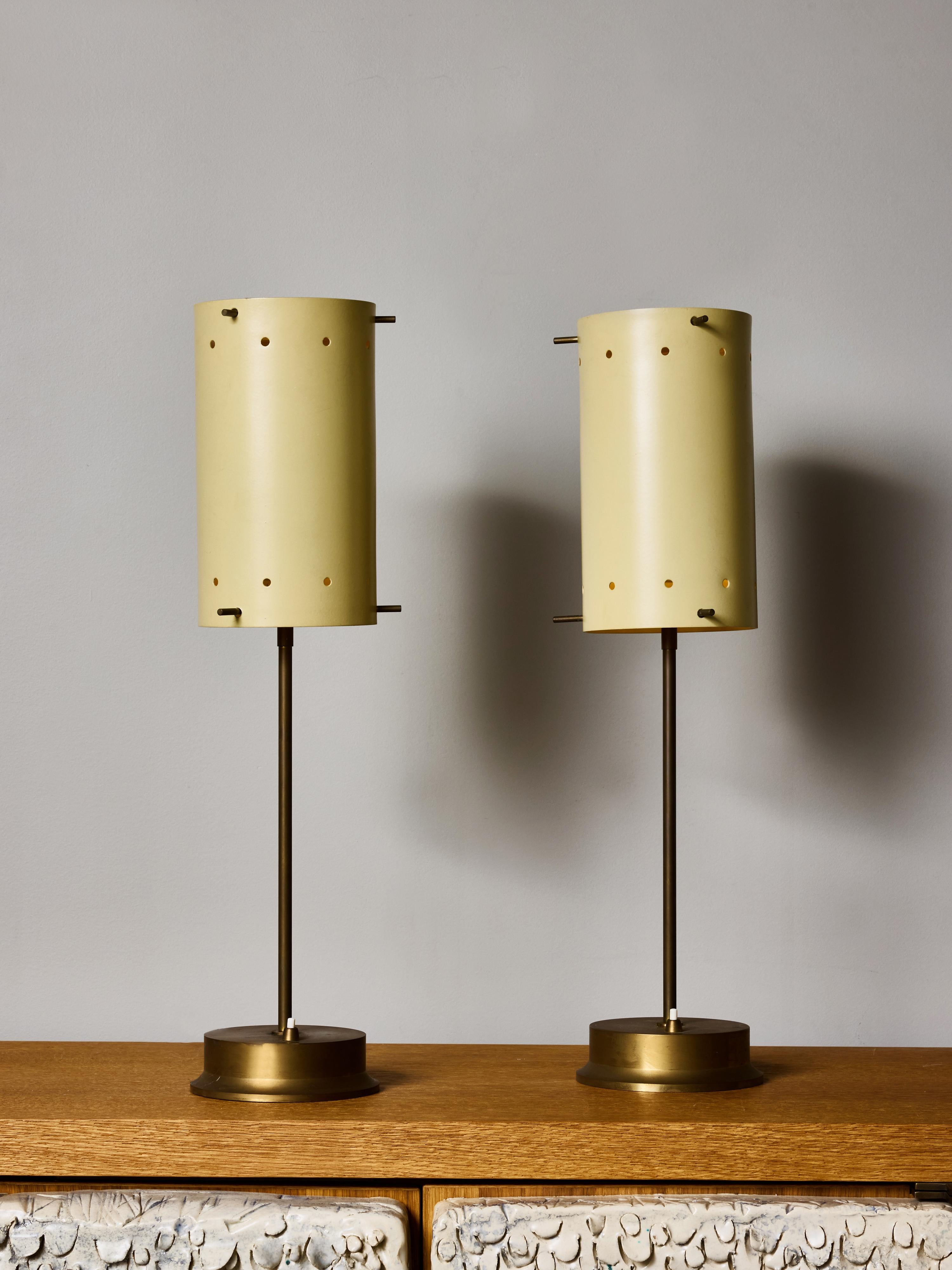 Paire de lampes de table modernes du milieu du siècle, dotées d'élégants corps en laiton et d'abat-jours cylindriques sculpturaux en métal peint. La douce finition crème dorée des teintes est ponctuée d'un motif rythmique de petites perforations