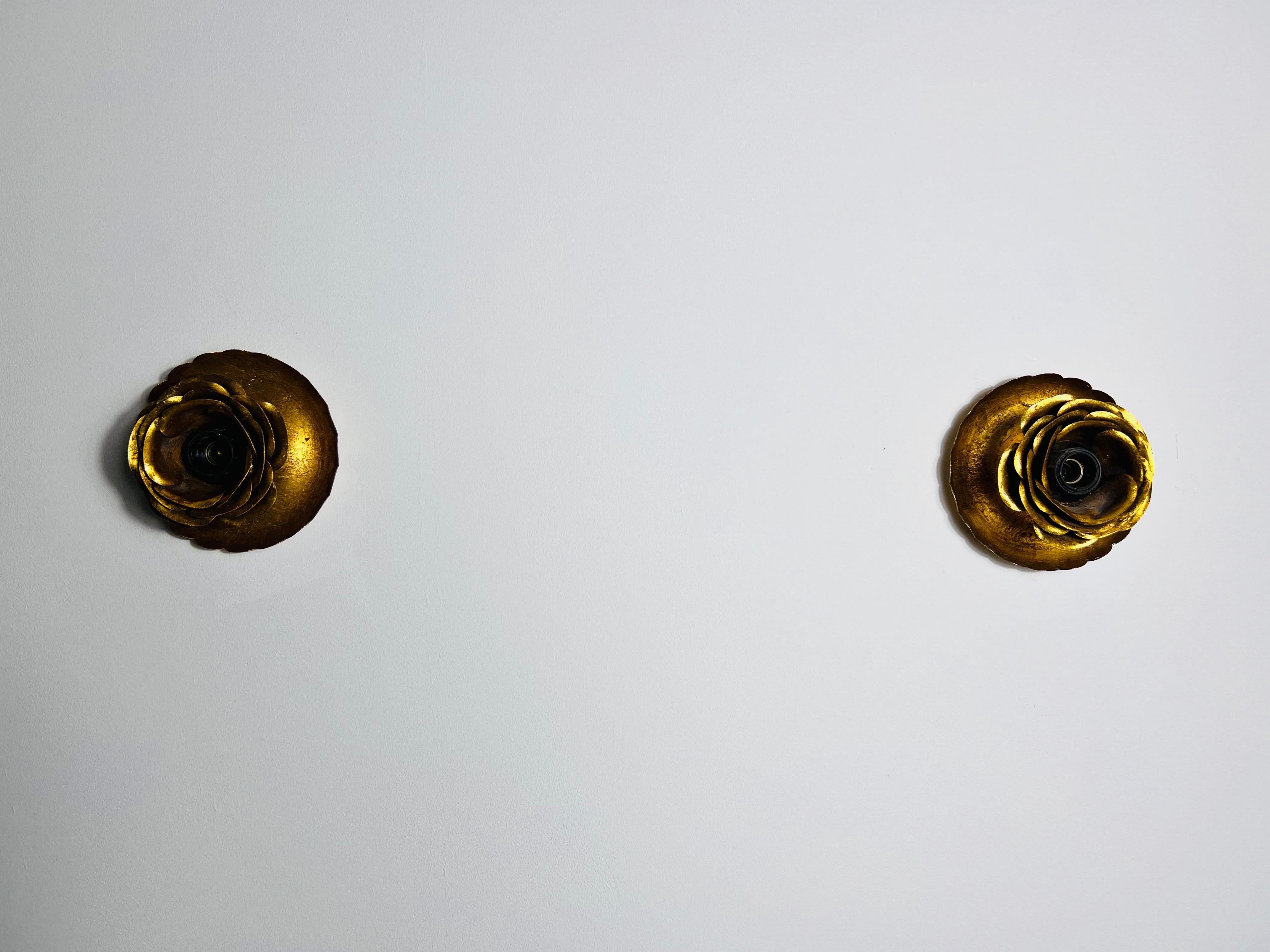 This exquisite pair of brass wall lamps from the 1960s exudes elegance and charm. Designed in the shape of a rose, the bulb is nestled at the center, creating a harmonious and idyllic aesthetic.

The design beautifully blends influences of Hollywood