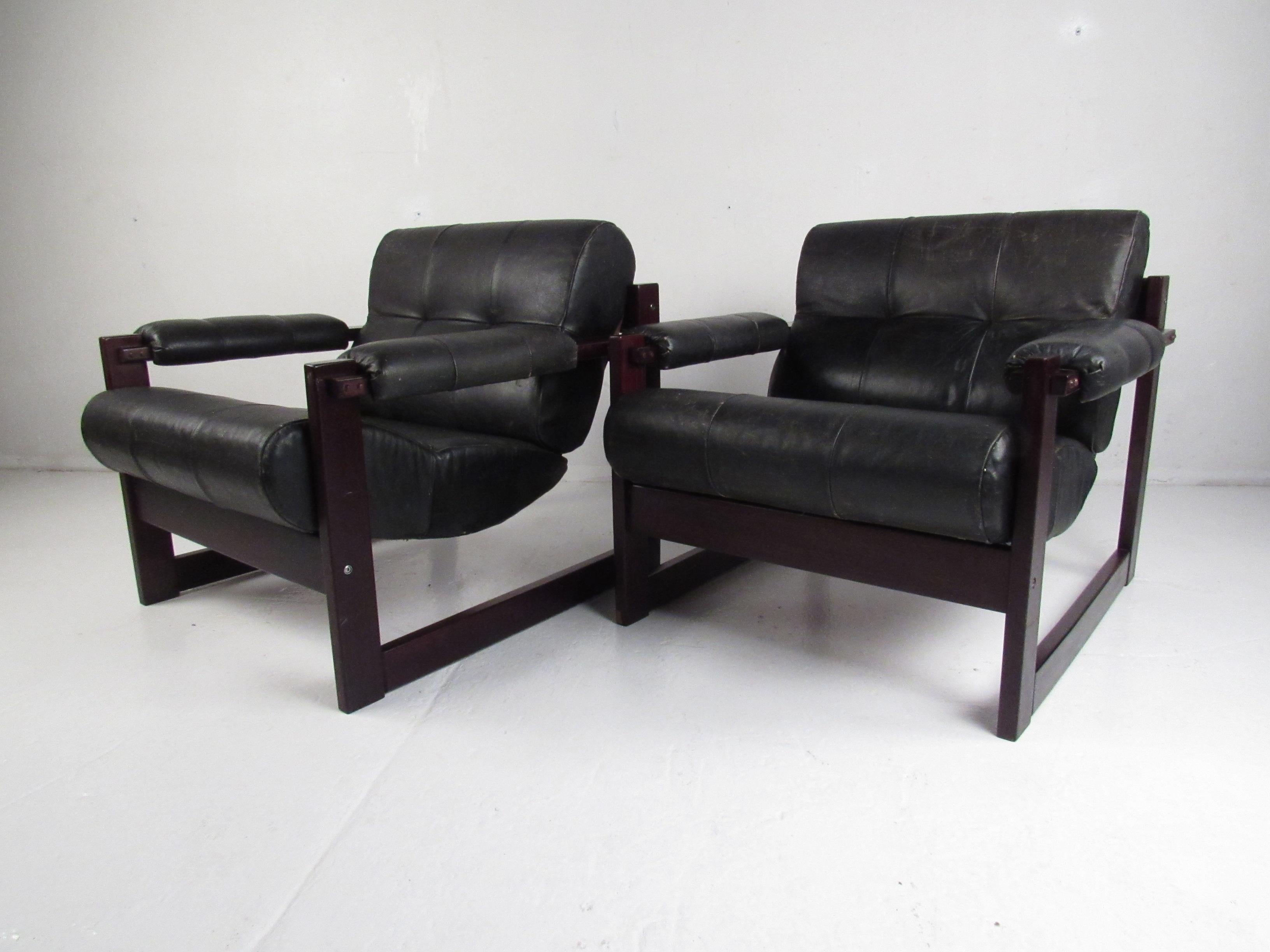 This stunning pair of vintage modern lounge chairs boast sturdy rosewood frames and black leather upholstery. A sleek hammock style design with squared off sides that function as the armrest and the sled legs. This comfortable lounge chair has thick