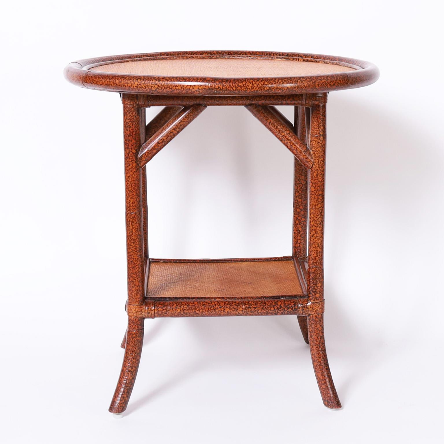 Pair of British Colonial style stands or tables with faux bamboo frames having a faux tortoise finish and with round tops and lower tier covered with grasscloth.