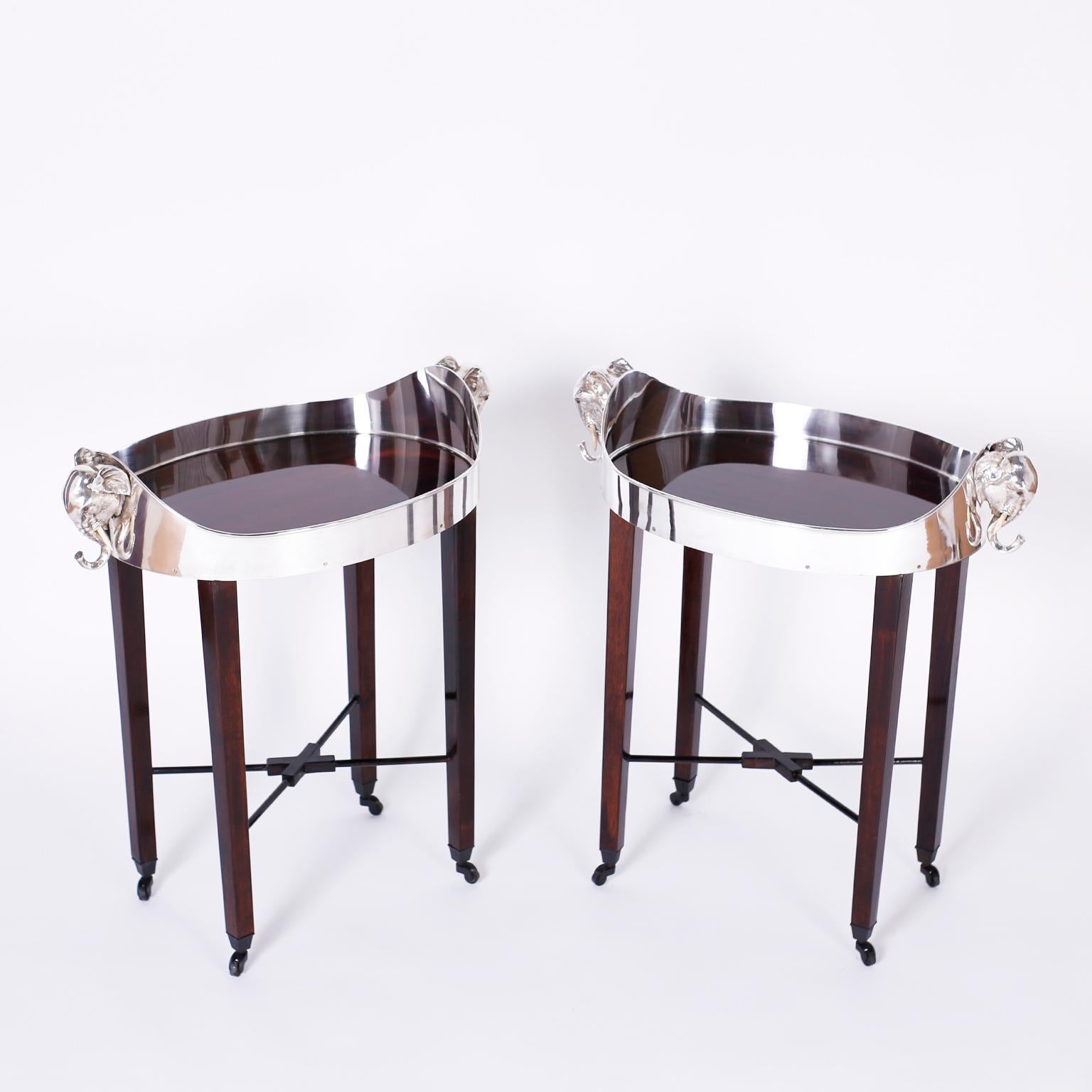 Impressive pair of vintage British colonial style trays presented on contemporary legs, featuring vintage silvered metal galleries with elephant head handles around a mahogany surface. The mahogany elegant tapered legs have cross stretchers and are
