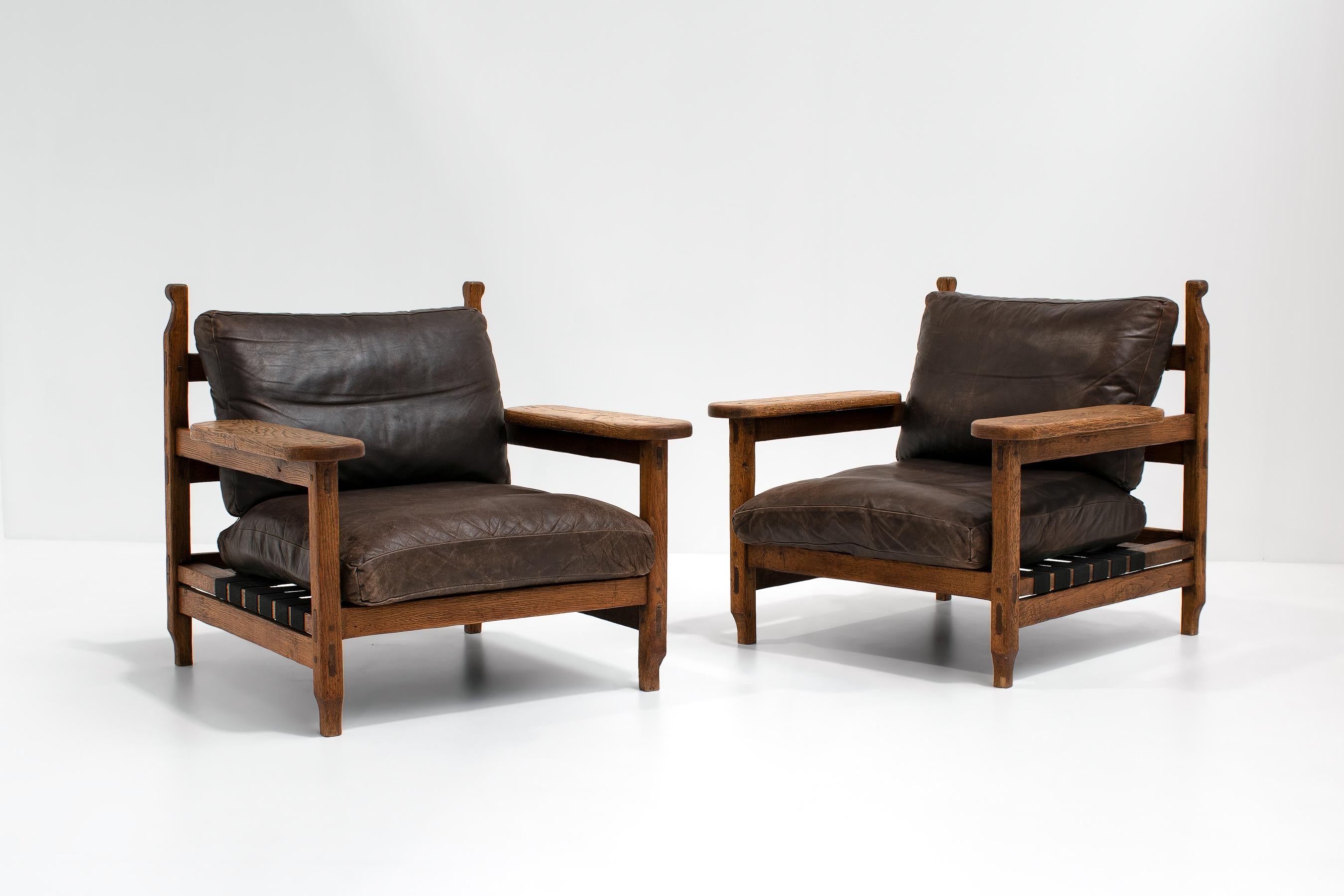 Unique pair of chunky brutalist lounge chairs in leather and oak, 1970s. Sourced in France.

Beautifully carved sculptural wooden frame in combination with thick brown patinated and original leather. 

Both chairs were left in their original