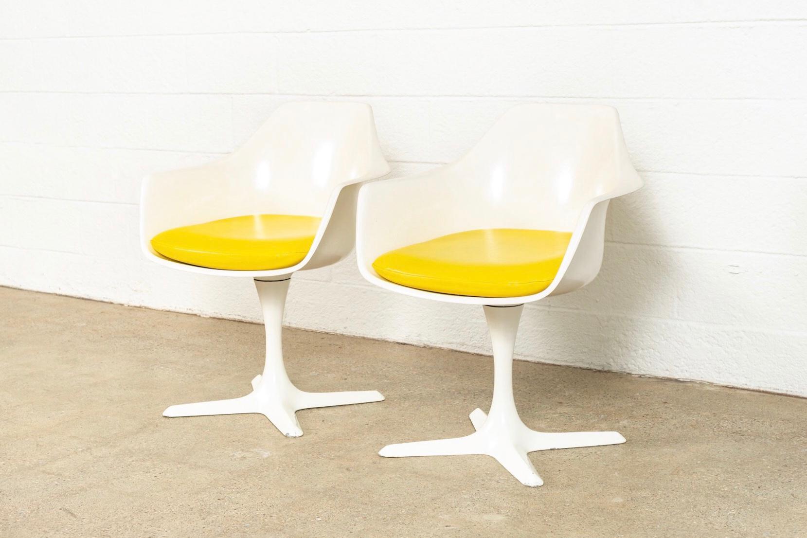 This pair of vintage Mid-Century Modern Burke tulip chairs in the style of Eero Saarinen are circa 1960. The iconic tulip design has clean lines and elegant curves. This set of armchairs features a white molded fiberglass seat form on a 360 degree