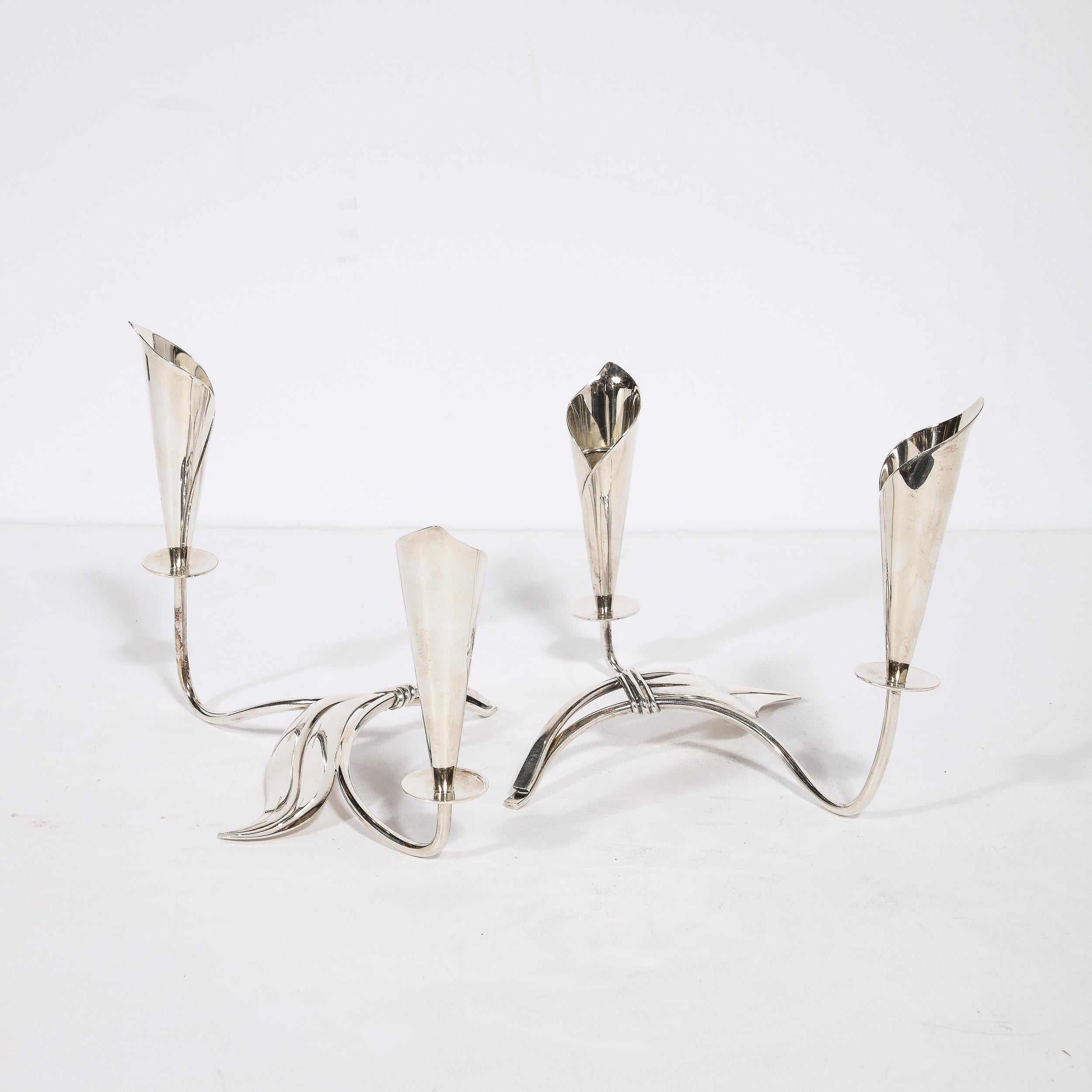 This elegant pair of Mid-Century Modern silver plate Cala Lily candle holders were realized in Denmark by the esteemed maker Hans Jensen circa 1960. They offer stylized and subtly abstracted interpretations of the iconic flower- the cala lily-